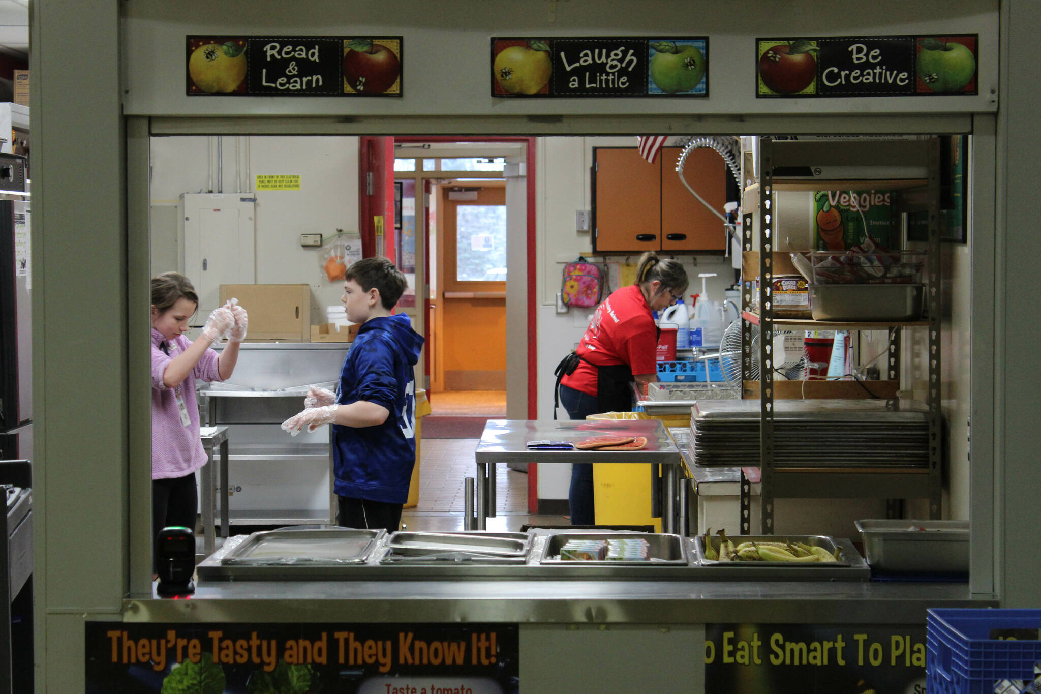 From left: sixth graders Katelynn Albritton and Ford Jacobson assist Kitchen Manager Toni Buchanan in the cafeteria at Sterling Elementary School on Thursday, Nov. 10, 2022, in Sterling, Alaska. (Ashlyn O’Hara/Peninsula Clarion)