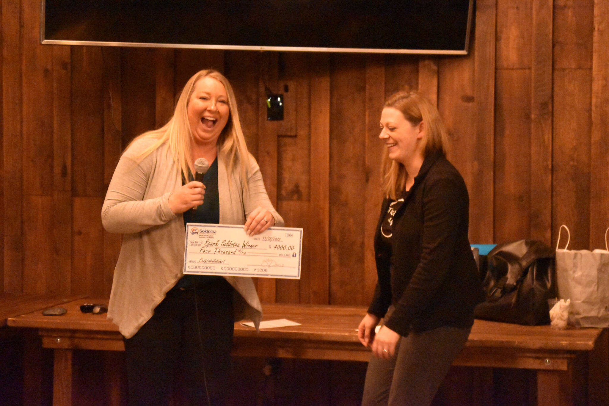 Jill Schaefer, one of the sharks, presents Anna Mercier with a novelty check for $4000 at the Spark Soldotna Shark Tank Event on Friday, Nov. 18, 2022, at The Lone Moose Lodge in Soldotna, Alaska. (Jake Dye/Peninsula Clarion)