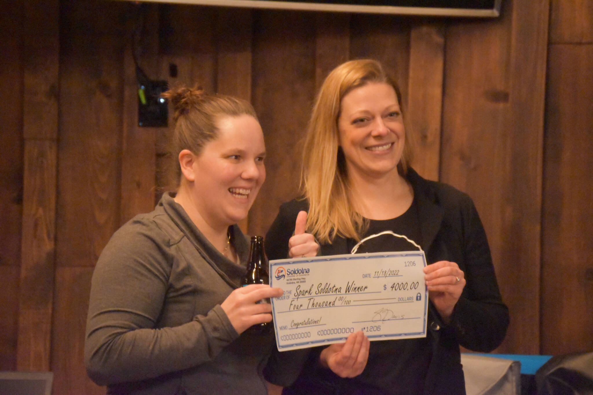 Top winners Samantha Pyfer and Anna Mercier are seen with a novelty check for $4000 at the Spark Soldotna Shark Tank Event on Friday, Nov. 18, 2022, at The Lone Moose Lodge in Soldotna, Alaska. (Jake Dye/Peninsula Clarion)