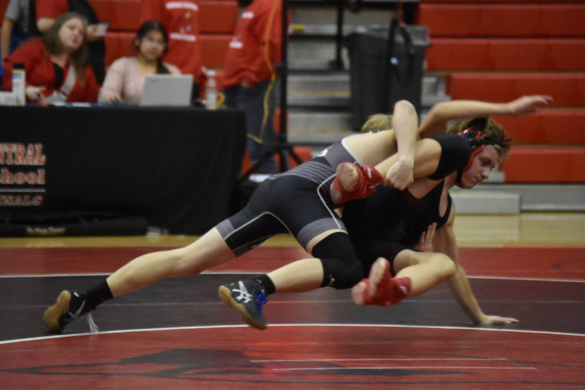 Nikiski’s Thayne Quiner leaps into a grab on Kenai’s Bishop Andruss during a dual meet on Tuesday, Nov. 29, 2022, at Kenai Central High School in Kenai, Alaska. (Jake Dye/Peninsula Clarion)