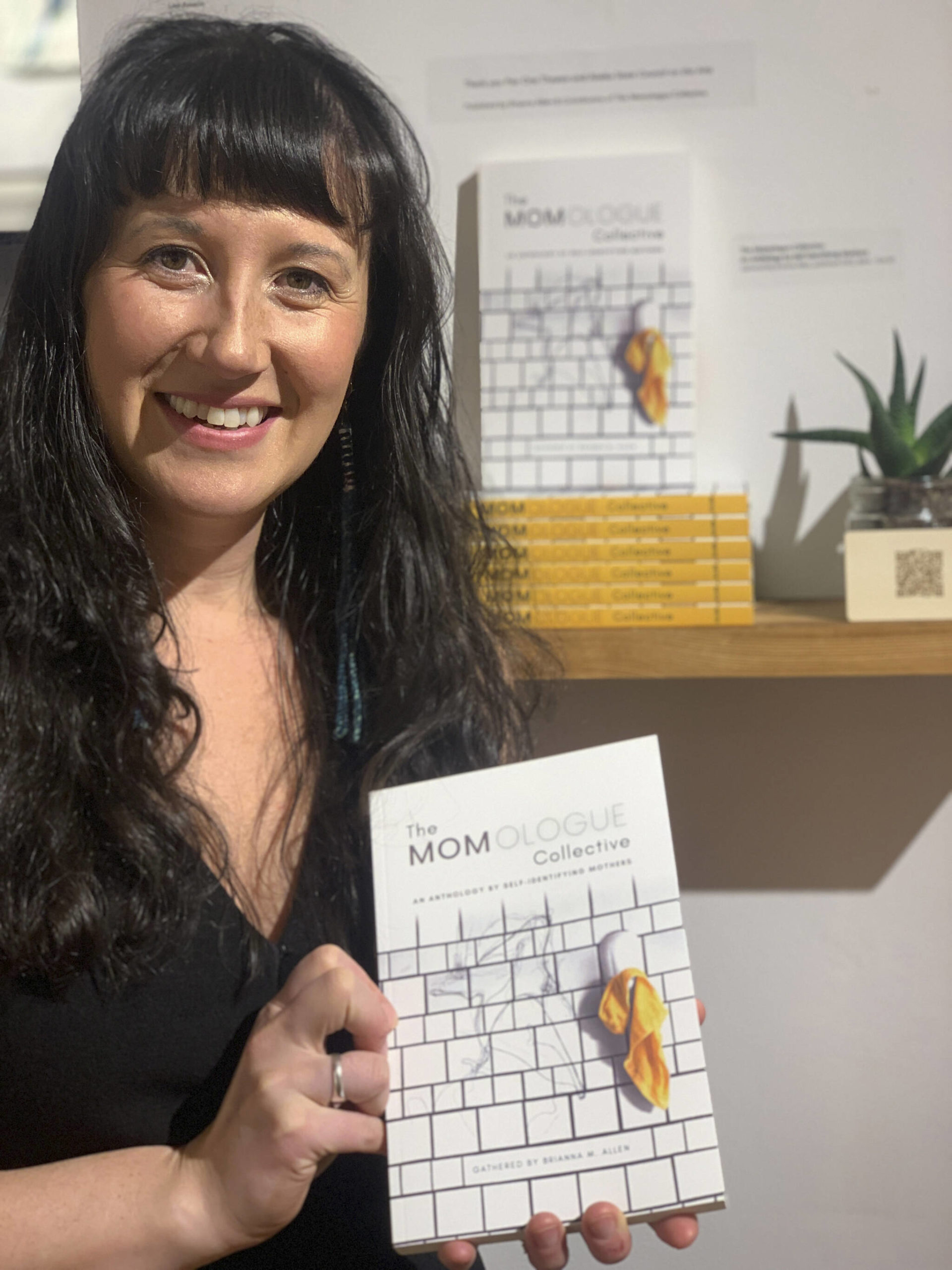Brianna Allen poses with the book she edited, The MOMologues, at the opening of the Mother exhibit showing this month at Bunnell Street Arts Center. (Photo by Christina Whiting)