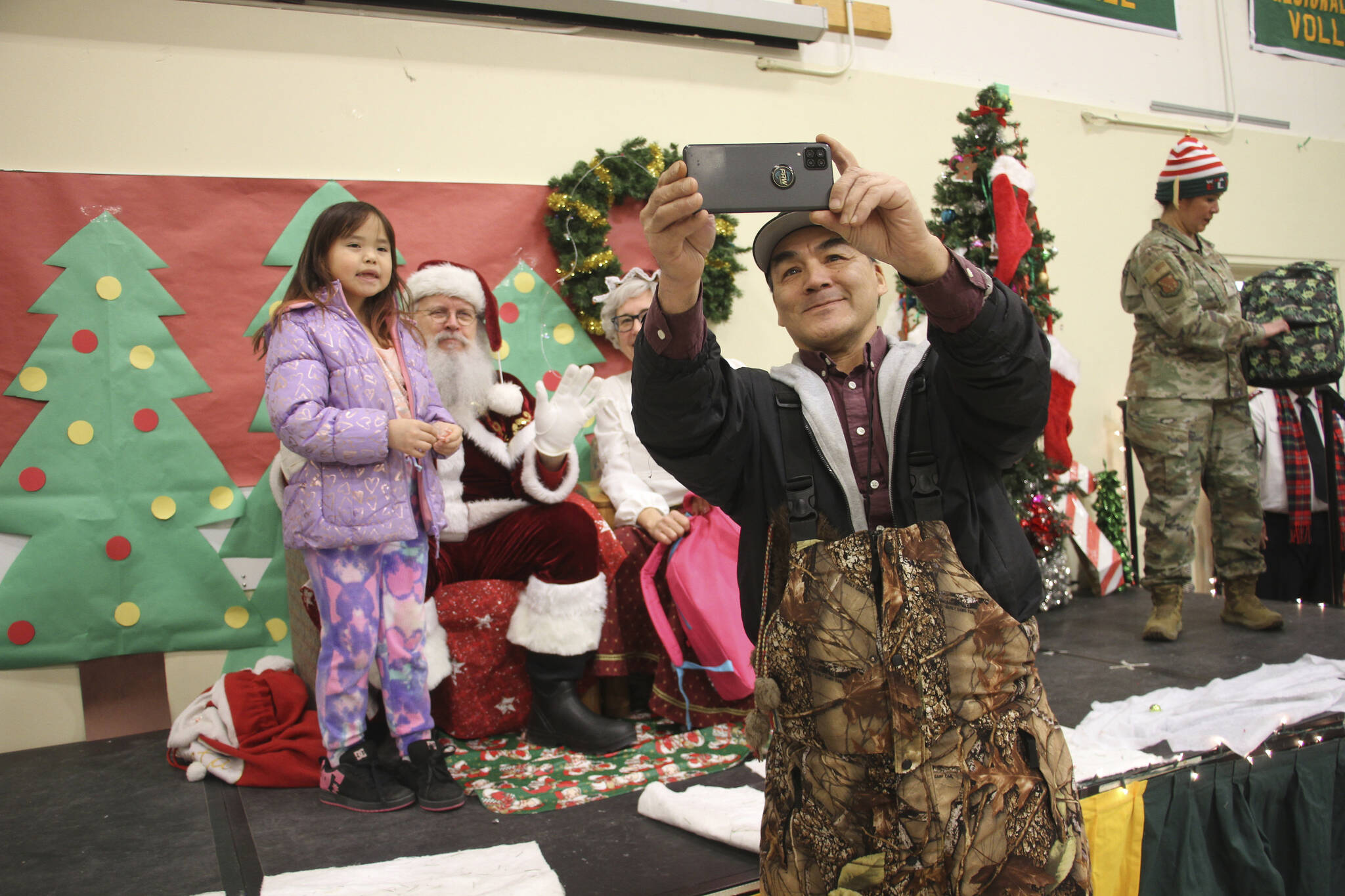 A parent takes a selfie with a child and Santa and Mrs. Claus in Nuiqsut, Alaska, on Nov. 29, 2022. Operation Santa Claus, the Alaska National Guard’s outreach program, attempts to bring Santa and Mrs. Claus and gifts to children in two or three Alaska Native villages each year, including Nuiqsut in 2022. (AP Photo/Mark Thiessen)