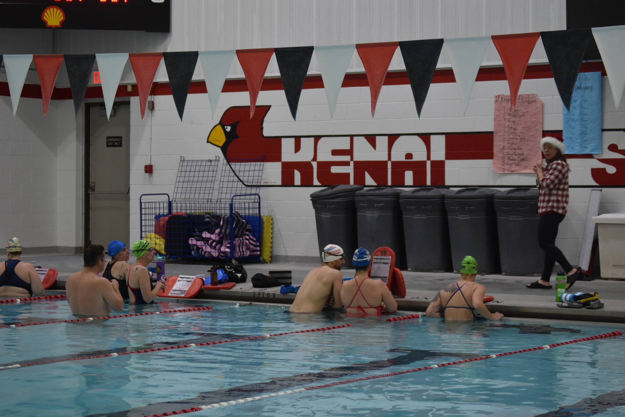 Swimmers gather at the wall to receive their next workout set from Coach Angie Brennan during a Top of the World Swimming practice on Wednesday, Dec. 14, 2022, at Kenai Central High School in Kenai, Alaska. (Jake Dye/Peninsula Clarion)