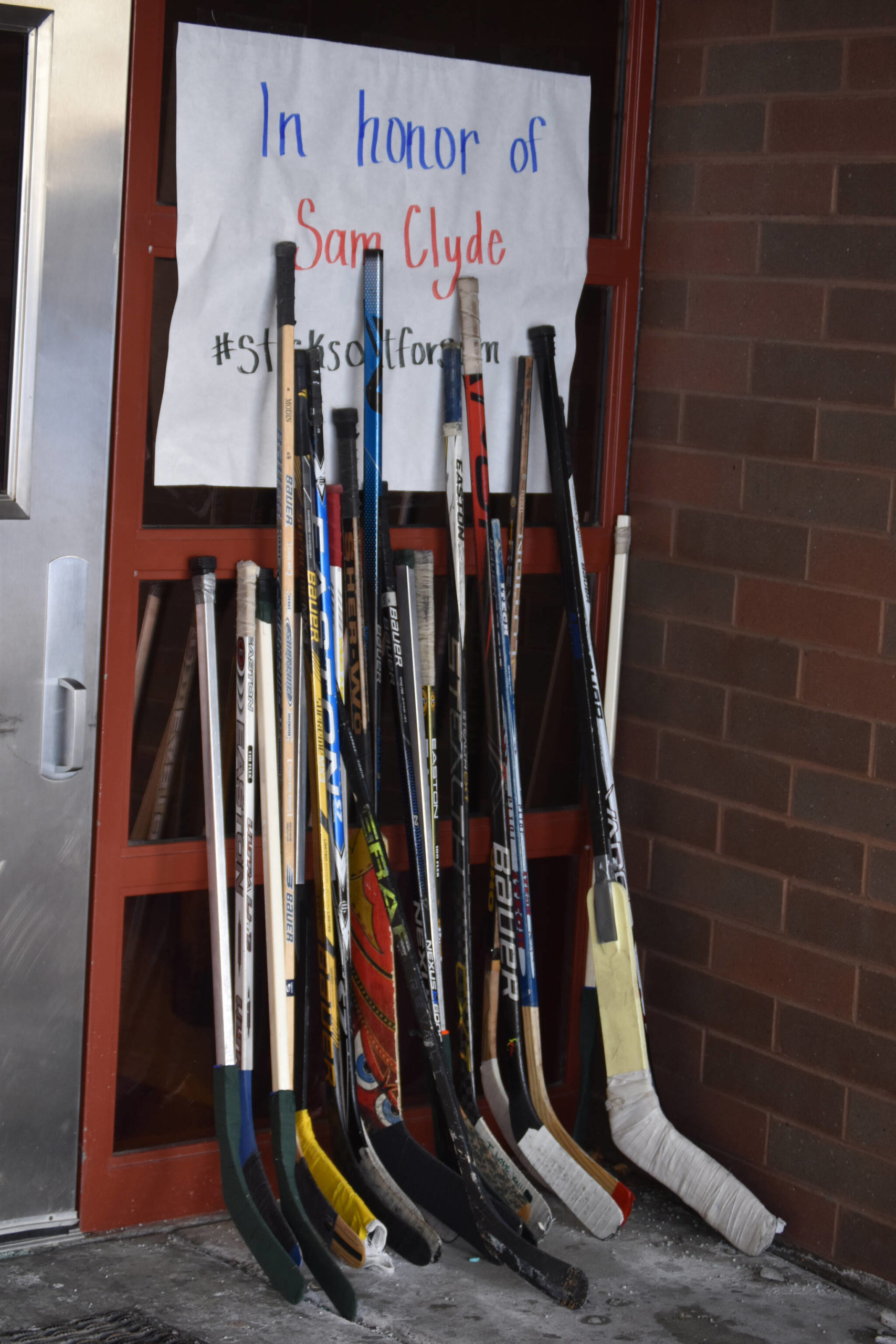 A collection of hockey sticks sit outside in honor of Sam Clyde on Friday, Dec. 16, 2022, at Skyview Middle School in Soldotna, Alaska. (Jake Dye/Peninsula Clarion)