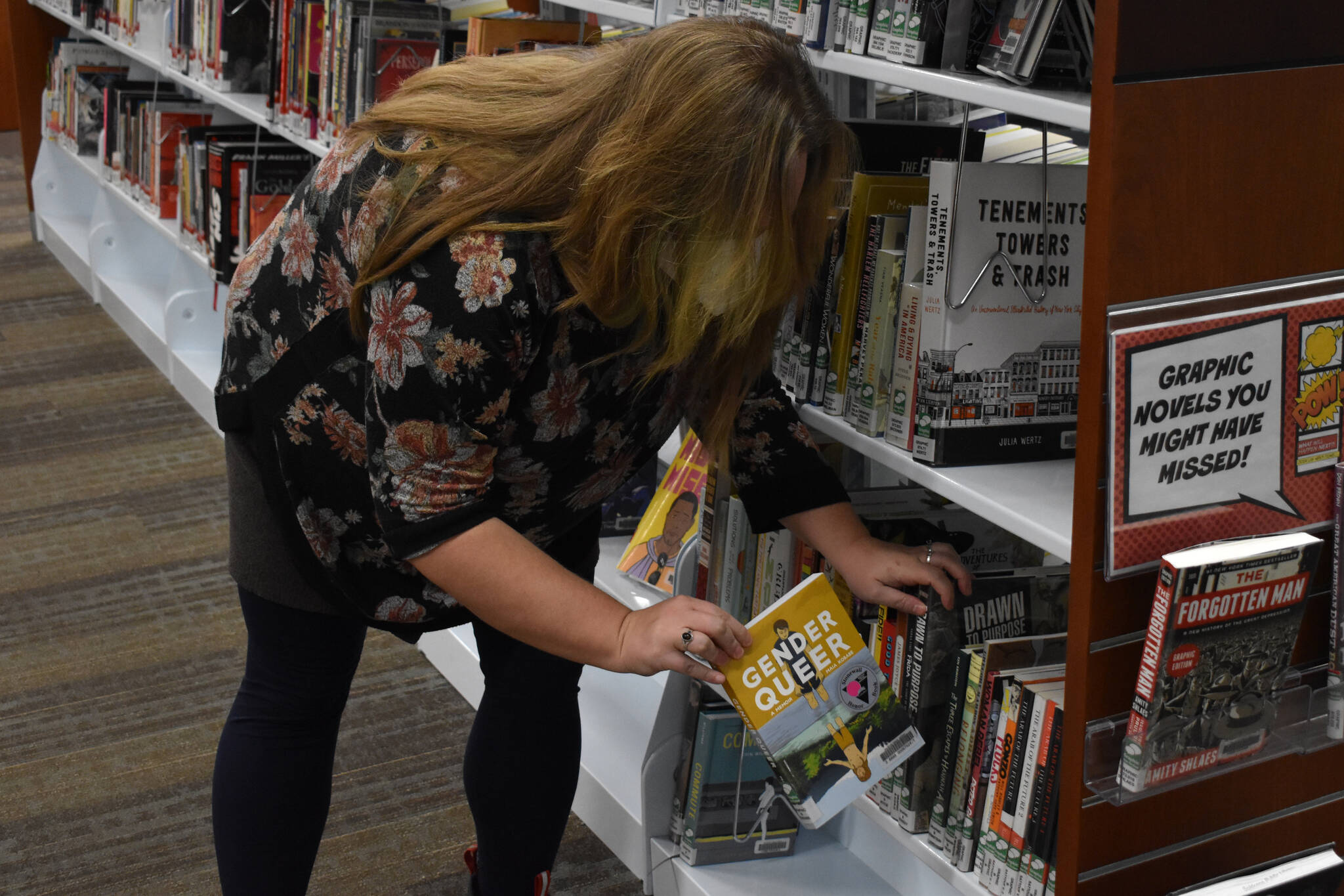 Jake Dye / Peninsula Clarion 
Ryanna Thurman, assistant Soldotna Public Library director, pulls a copy of “Gender Queer: A Memoir” by Maia Kobabe from the shelves on Tuesday, Below, examples of contemporary books that have been banned or challenged in recent years are displayed at the library on Sept. 24.