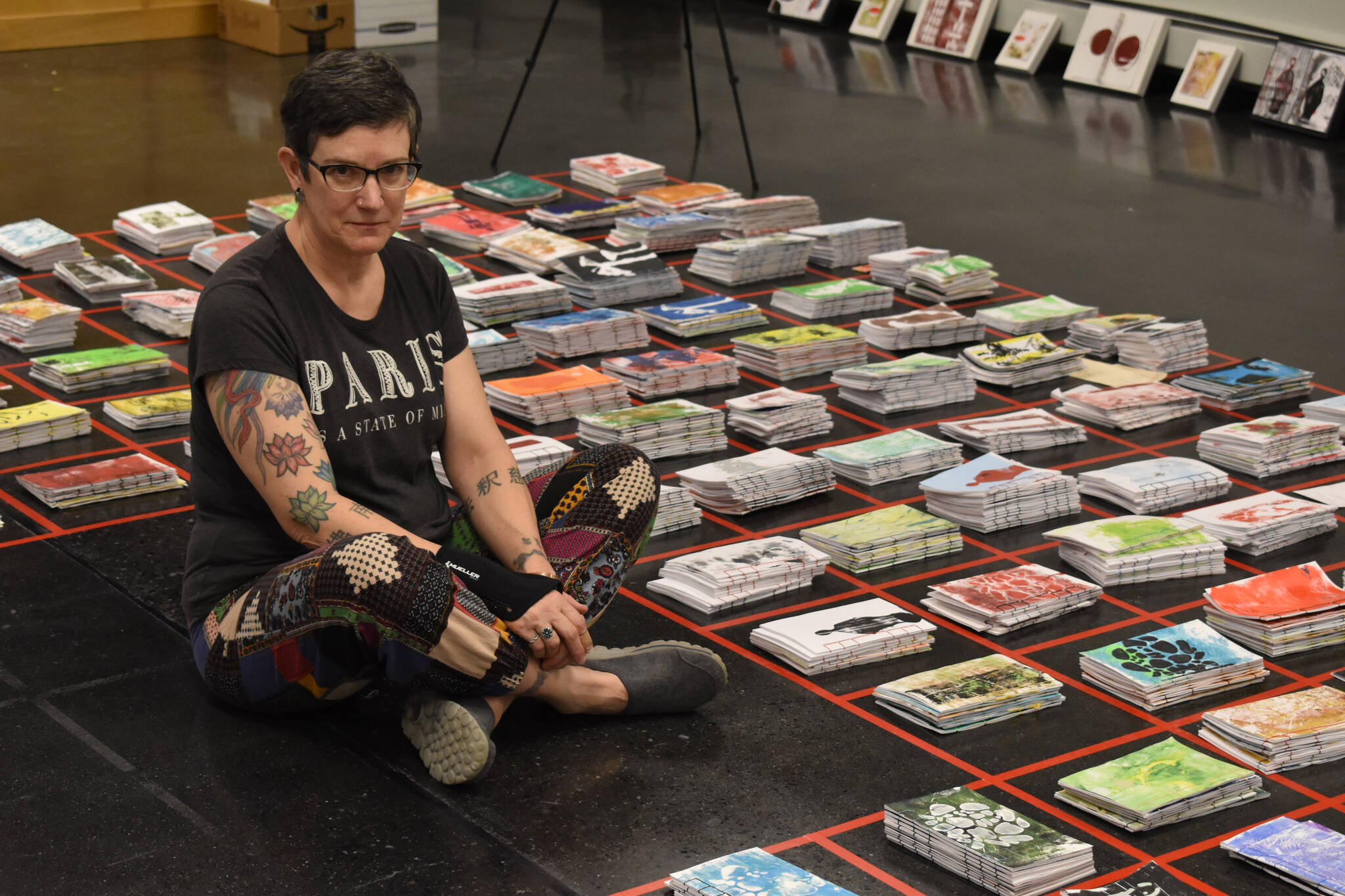 Diane Dunn sits, surrounded by 2000 journals she made and painted by hand, on Tuesday, Jan. 3, 2023, ahead of the opening of “2000 Journals: Filling the Void” at the Kenai Art Center in Kenai, Alaska. (Jake Dye/Peninsula Clarion)