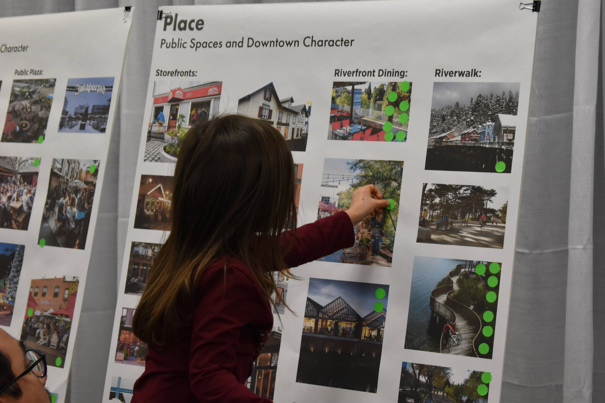 A young girl is lifted to place a sticker indicating her preference on a concept board on Thursday, Jan. 12, 2023, at the Soldotna Riverfront Redevelopment Open House at the Soldotna Regional Sports Complex in Soldotna, Alaska. (Jake Dye/Peninsula Clarion)