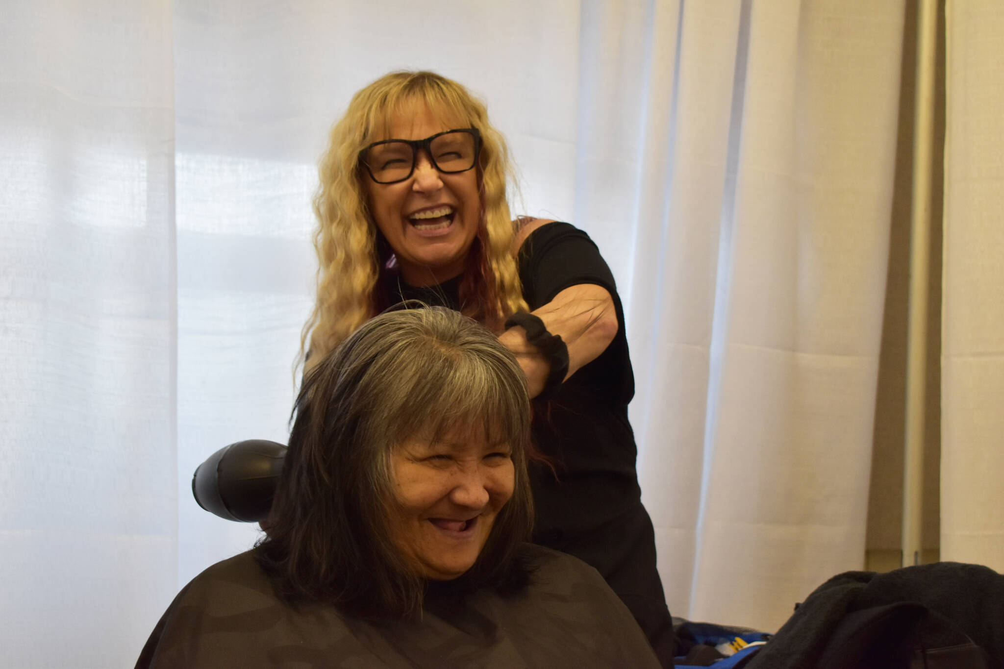 Tamera Mapes and a client laugh and joke with one another during a free haircut at Project Homeless Connect on Tuesday, Jan. 31, 2023, at the Soldotna Regional Sports Complex in Soldotna, Alaska. (Jake Dye/Peninsula Clarion)