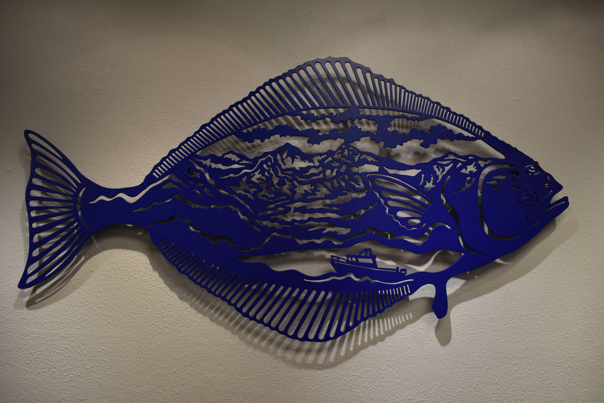 A metal halibut containing a mountain range seen from the Homer Spit, created by Chelline Larsen, hangs Tuesday, Jan. 31, 2023, at the Kenai Art Center, in Kenai, Alaska, as part of Metalwork & Play. (Jake Dye/Peninsula Clarion)