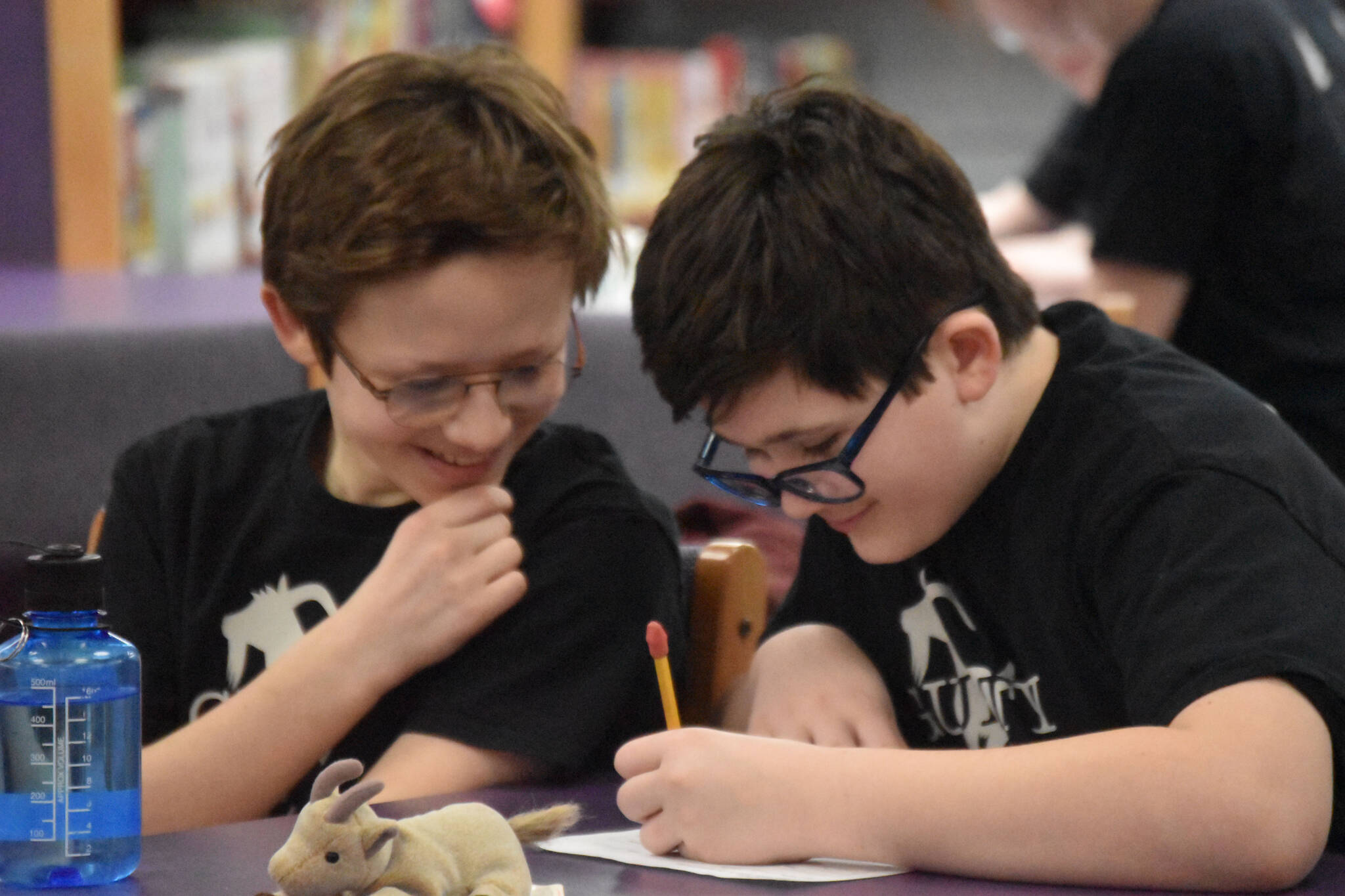 Luke Karpic and Oscar Marcou smile as they write their response to a question posed during Kenai Peninsula Borough School District Middle School Battle of the Books competition on Thursday, Feb. 9, 2023, at Kenai Middle School in Kenai, Alaska. (Jake Dye/Peninsula Clarion)