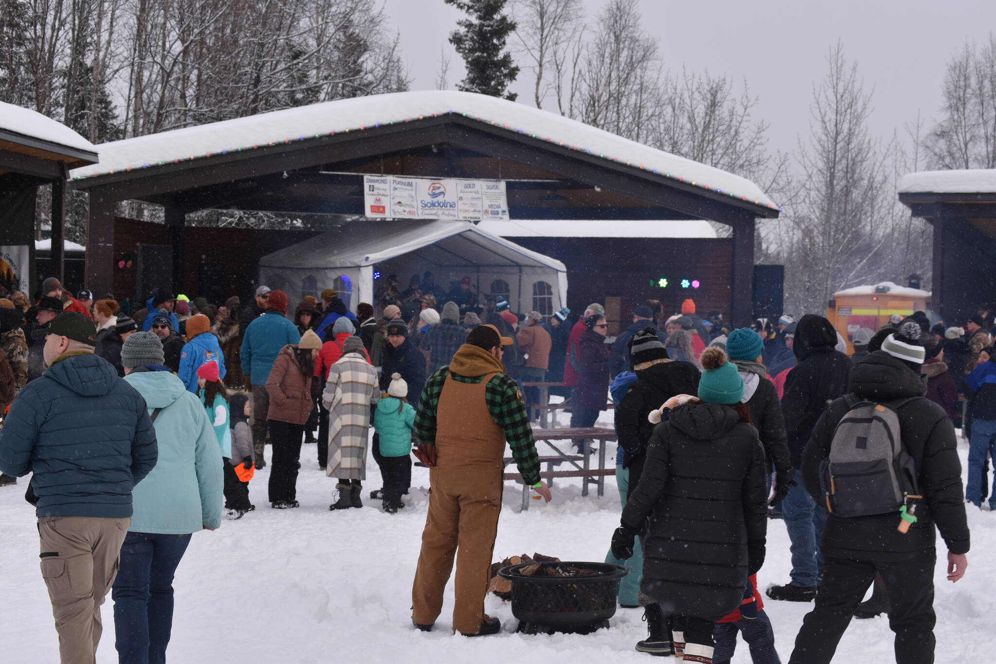 Snow falls as attendees of Frozen RiverFest gather around the stage and listen to The Ridgeway Rounders on Saturday, Feb. 18, 2023 at Soldotna Creek Park in Soldotna, Alaska. (Jake Dye/Peninsula Clarion)