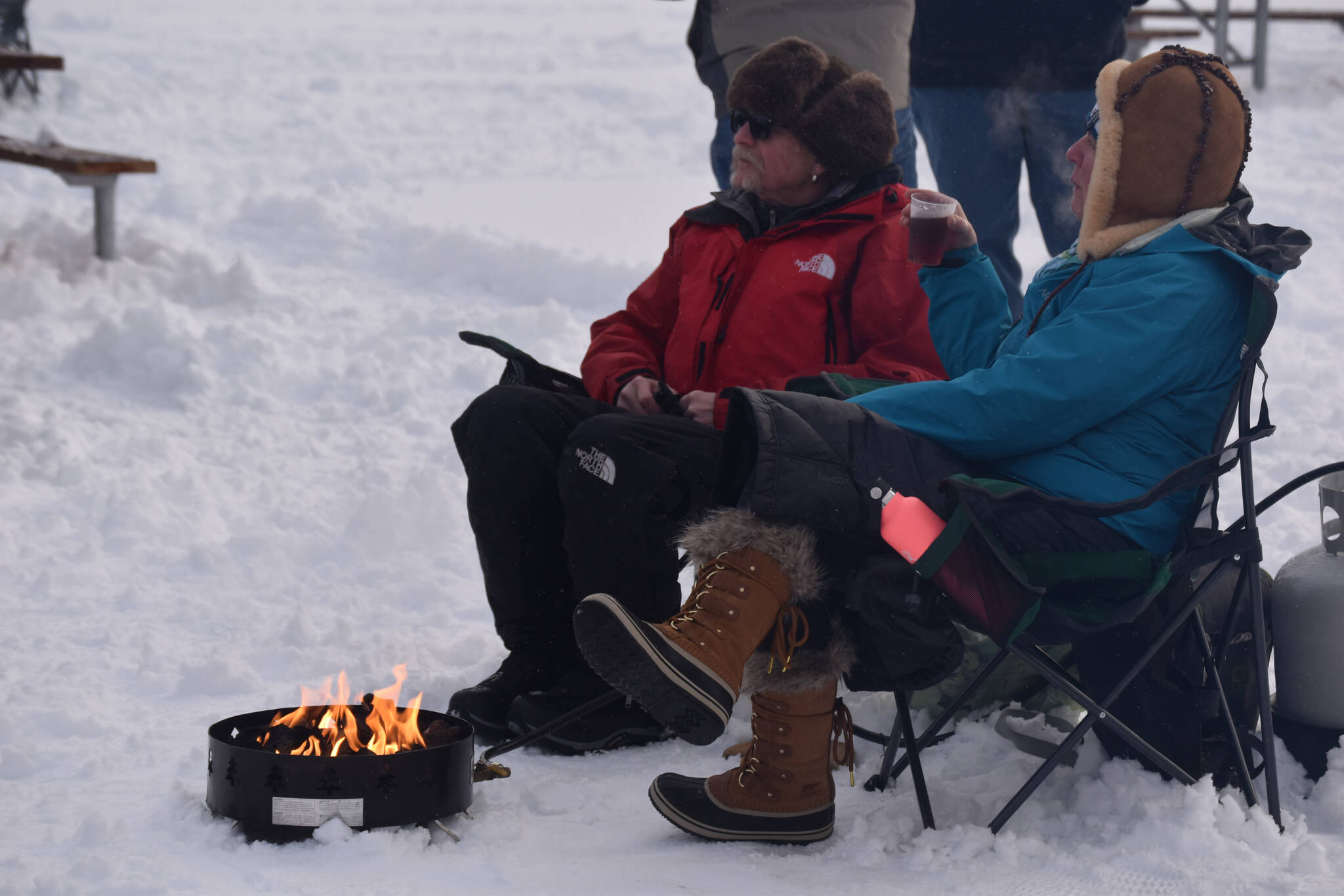 Attendees sip drinks and sit by the fire during Frozen RiverFest on Saturday, Feb. 18, 2023 at Soldotna Creek Park in Soldotna, Alaska. (Jake Dye/Peninsula Clarion)