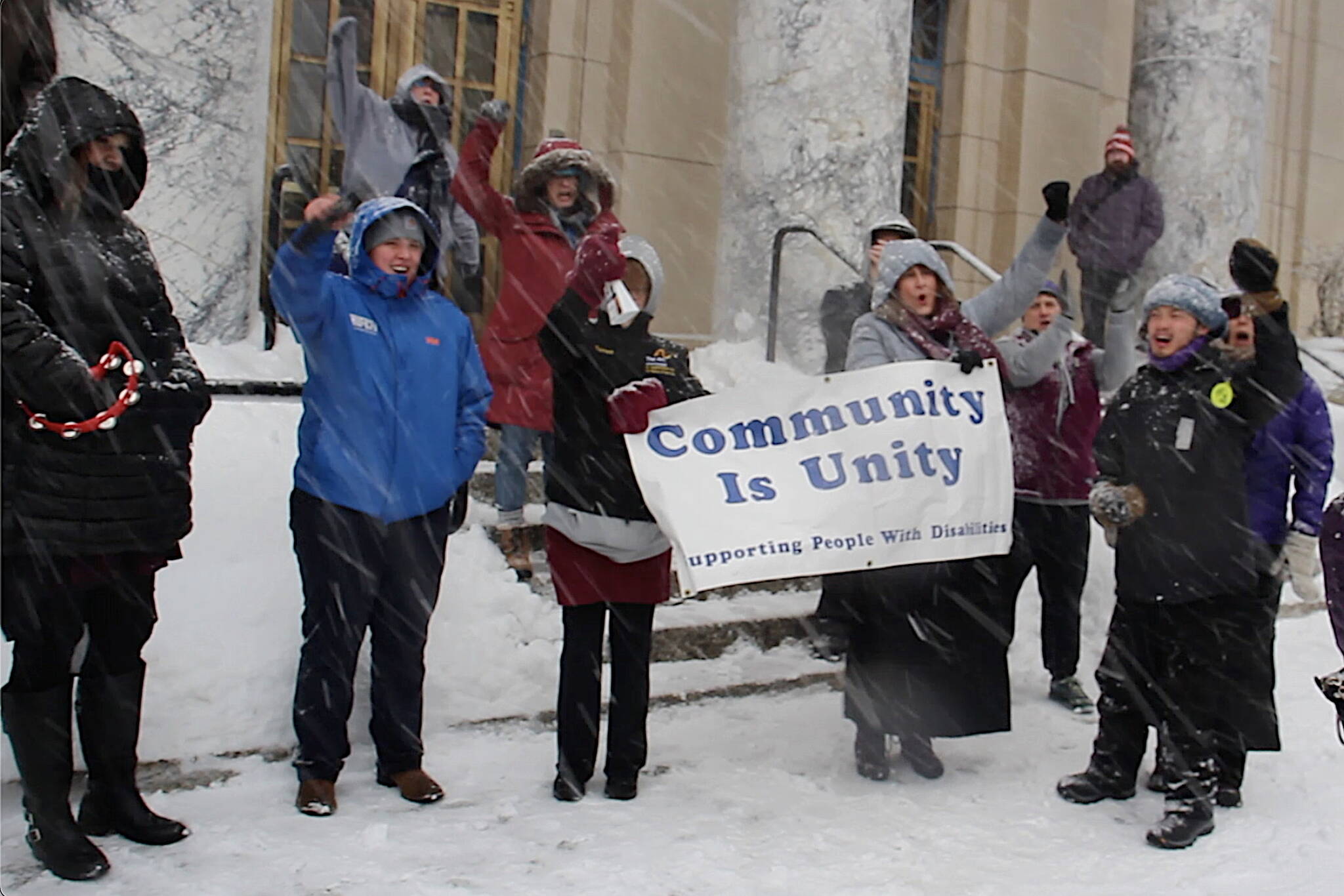 Mark Sabbatini / Juneau Empire
Alaska residents with disabilities and advocates providing services intended to support self-sufficiency wave a banner and noisemakers during a noontime Wednesday rally in a blizzard on the steps of the Alaska State Capitol.