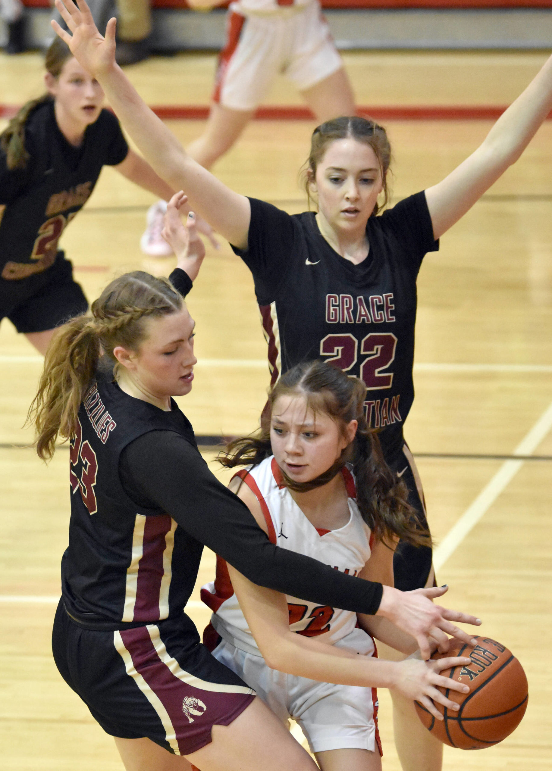 Kenai Central’s Emilee Wilson looks to escape the trap of Grace Christian’s Sophie Lentfer and Olivia Jones on Friday, March 3, 2023, at Kenai Central High School in Kenai, Alaska. (Photo by Jeff Helminiak/Peninsula Clarion)
