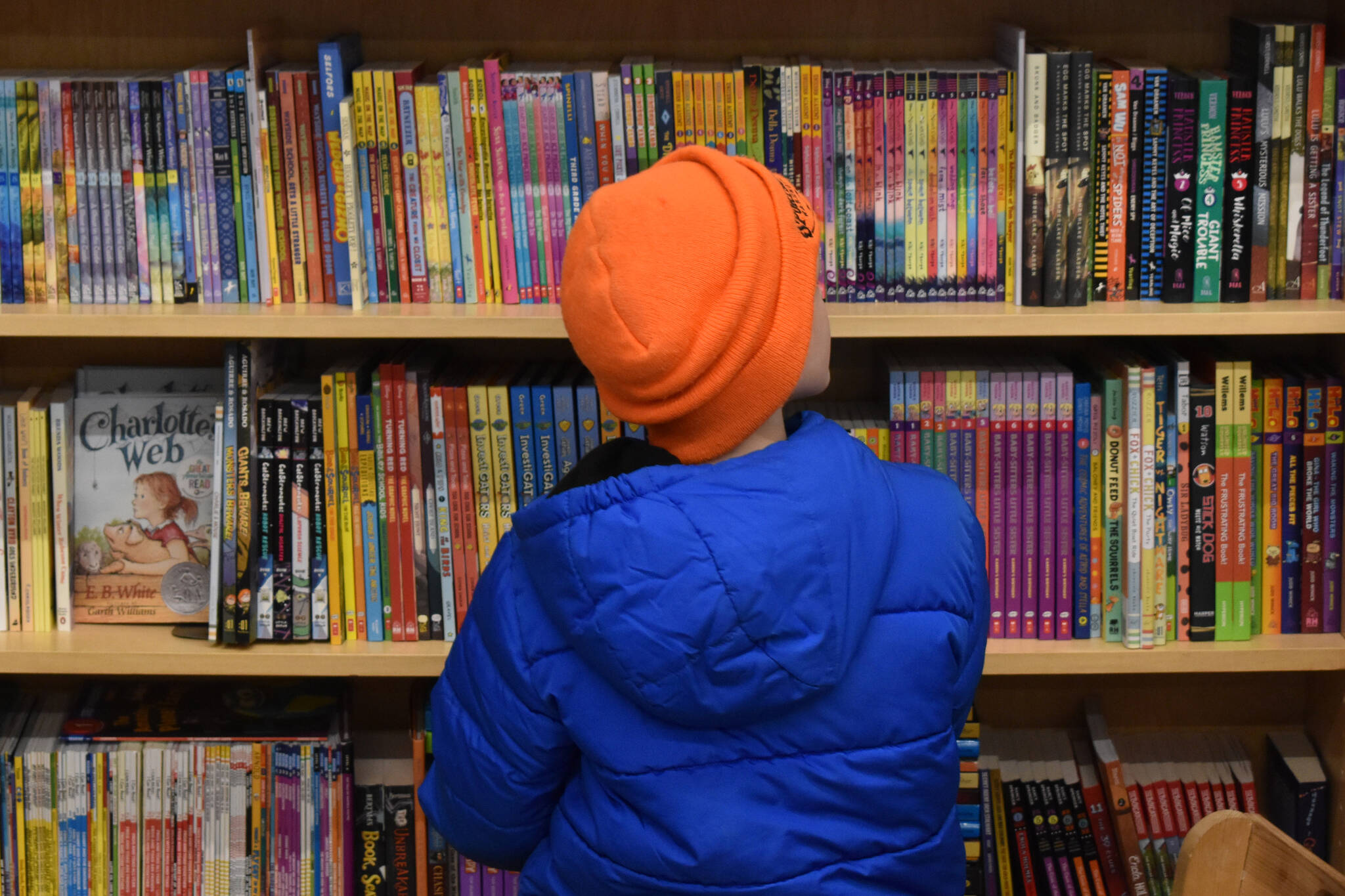 A Soldotna Elementary student weighs his options in front of shelves of books on Wednesday, March 8, 2023, at River City Books in Soldotna, Alaska. (Jake Dye/Peninsula Clarion)