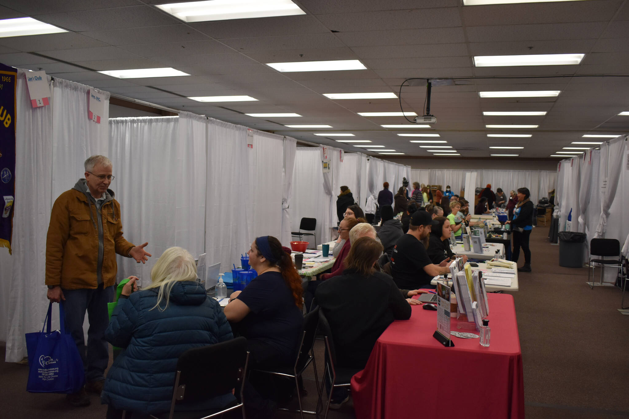 Volunteers sit at rows of tables or in curtained off booths during Project Homeless Connect on Tuesday, Jan. 31, 2023, at the Soldotna Regional Sports Complex in Soldotna, Alaska. (Jake Dye/Peninsula Clarion)