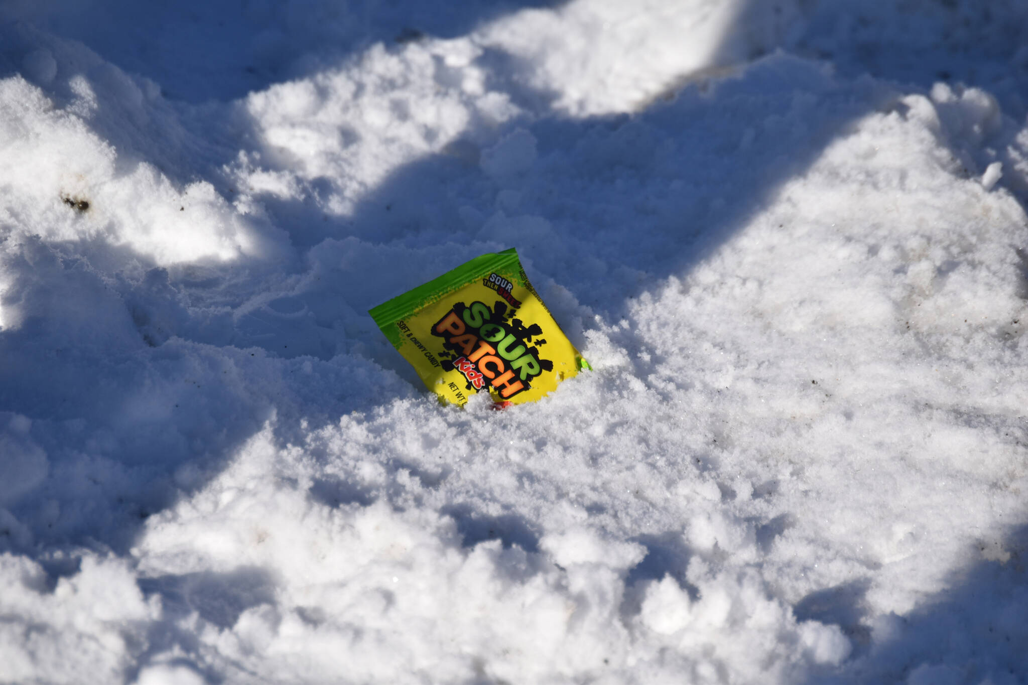 A bag of Sour Patch Kids rest in the snow as the 32nd annual Sweeney’s St. Patrick’s Day Parade proceeds down Fireweed Street in Soldotna, Alaska on Friday, March 17, 2023. (Jake Dye/Peninsula Clarion)