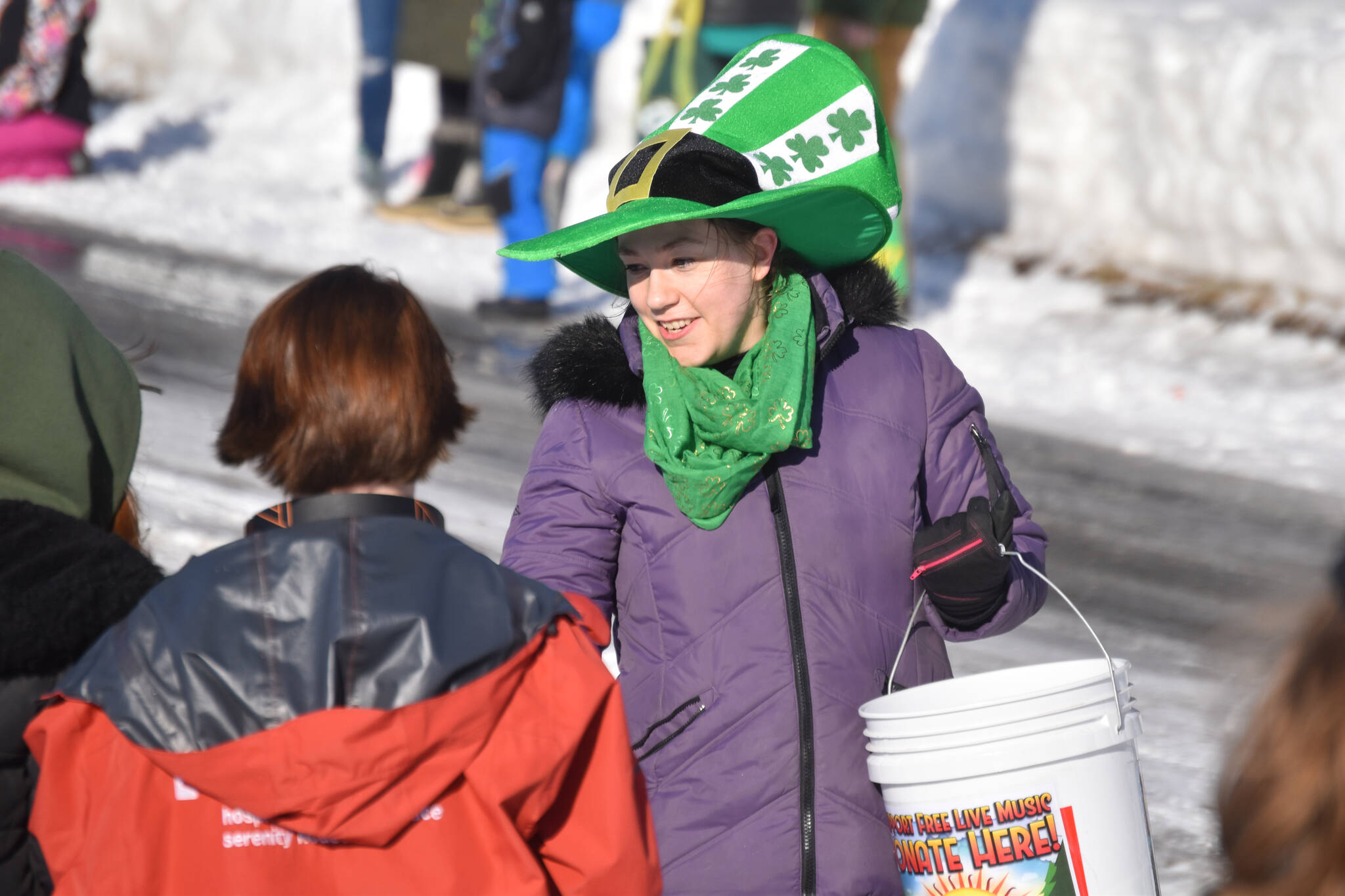 A woman in a big green hat passes out candy as the 32nd annual Sweeney’s St. Patrick’s Day Parade proceeds down Fireweed Street in Soldotna, Alaska on Friday, March 17, 2023. (Jake Dye/Peninsula Clarion)