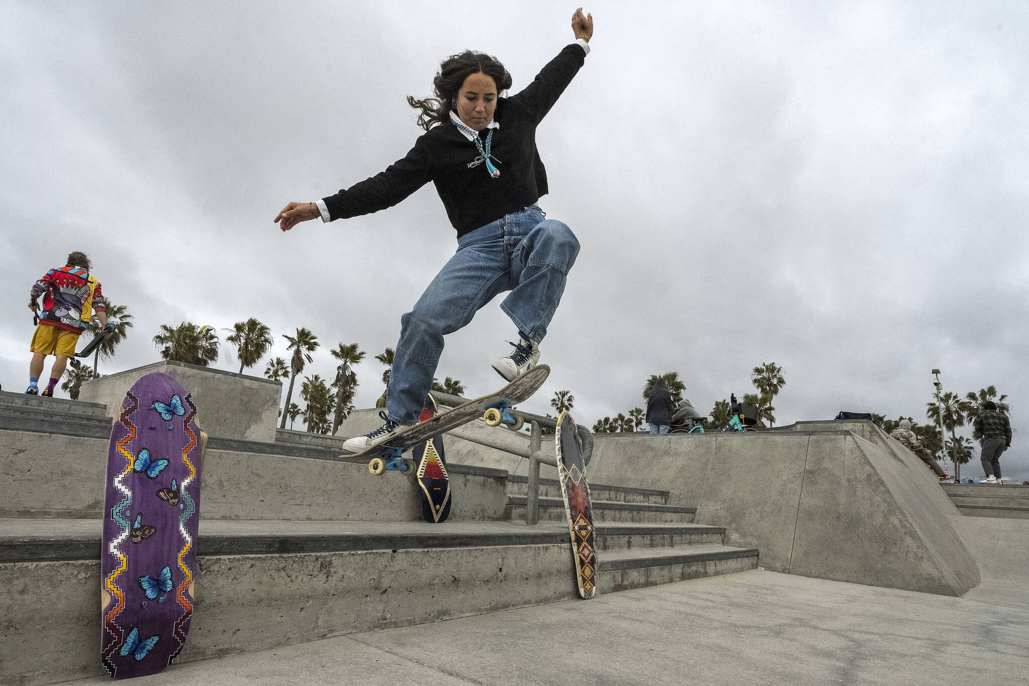 Expert skateboarder Di’Orr Greenwood, an artist born and raised in the Navajo Nation in Arizona and whose work is featured on the new U.S. stamps, rides her skateboard next to her artworks in the Venice Beach neighborhood in Los Angeles Monday, March 20, 2023. On Friday, March 24, the U.S. Postal Service is debuting the “Art of the Skateboard,” four stamps that will be the first to pay tribute to skateboarding. The stamps underscore how prevalent skateboarding has become, especially in Indian Country, where the demand for designated skate spots has only grown in recent years. (AP Photo/Damian Dovarganes)