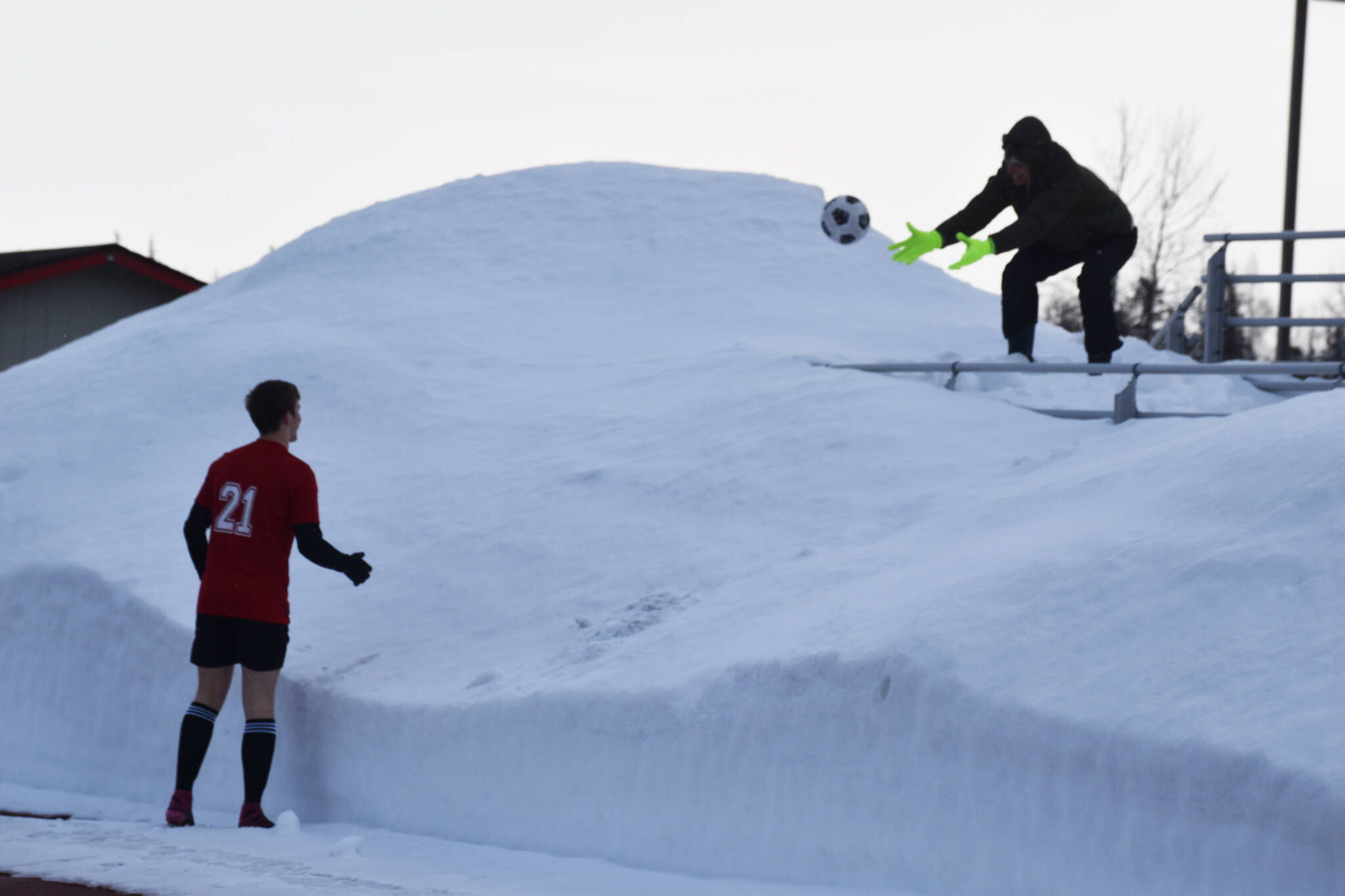 A spectator throws a ball lost in the snow back down to Bridger Beck during a soccer game at Ed Hollier Field in Kenai, Alaska, on Thursday, March 30, 2023. (Jake Dye/Peninsula Clarion)