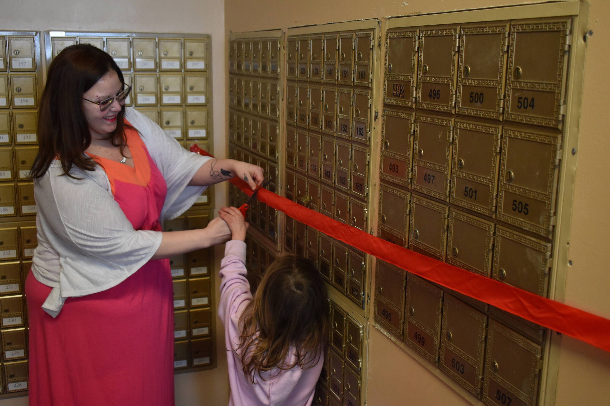 Jake Dye / Peninsula Clarion 
Monica Flores and Caia Bock cut a ribbon from the front of new post office boxes at Shipping Zone in Kenai on Saturday.