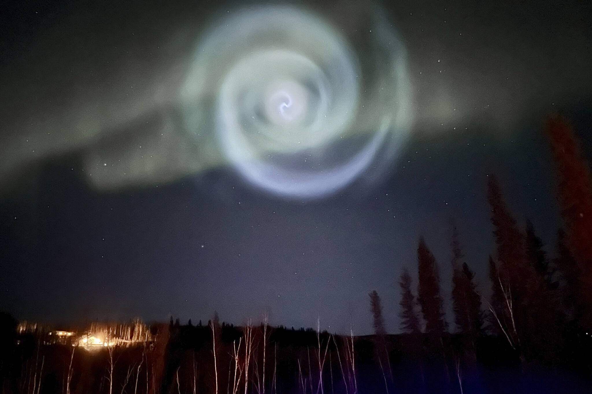 In this photo provided by Christopher Hayden, a light baby blue spiral resembling a galaxy appears amid the aurora for a few minutes in the Alaska skies near Fairbanks, Saturday, April 15, 2023. The spiral was formed when excess fuel that had been released from a SpaceX rocket that launched from California about three hours earlier turned to ice, and then the water vapor reflected the sunlight in the upper atmosphere. (Christopher Hayden via AP)