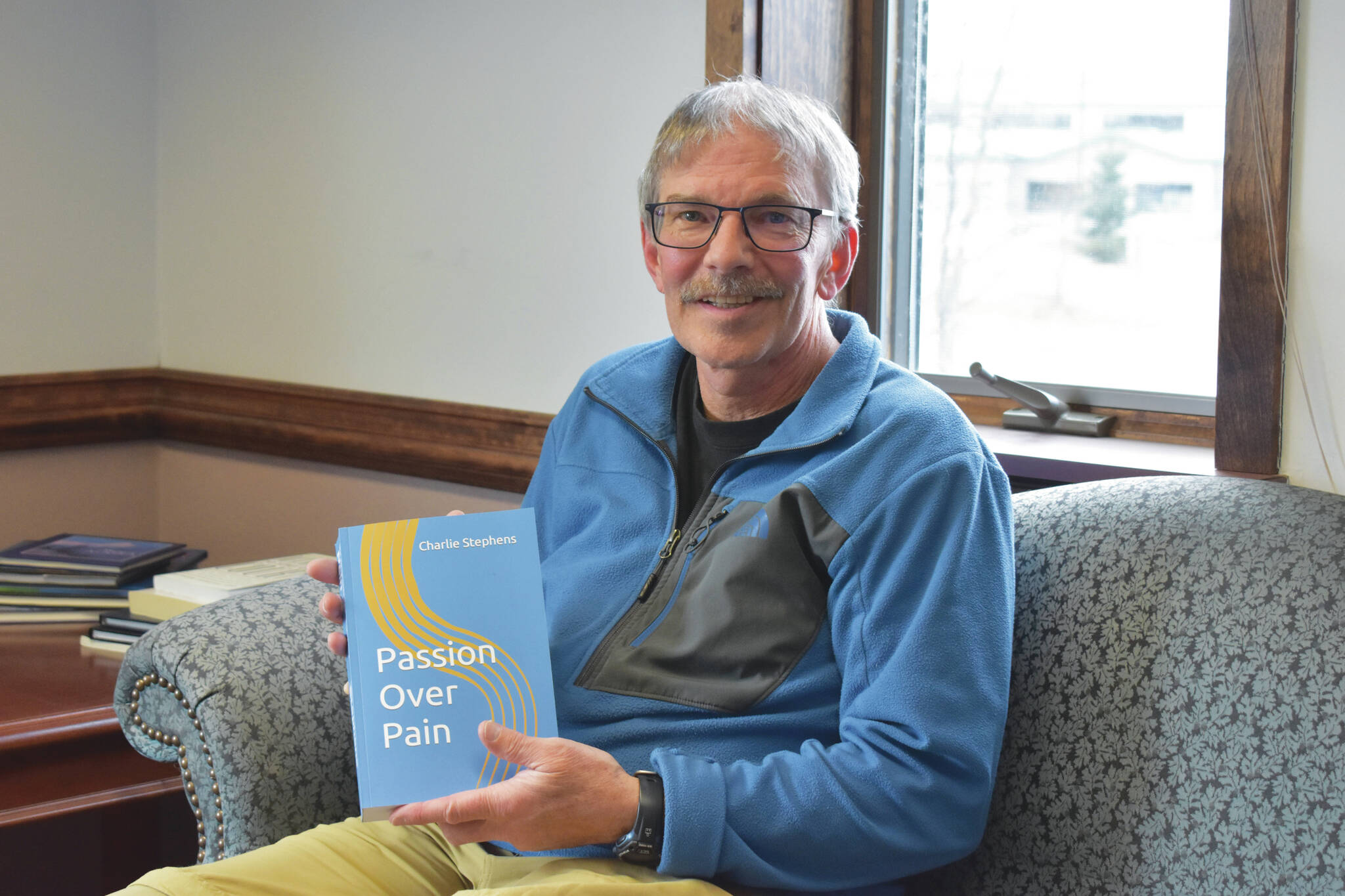 Jake Dye / Peninsula Clarion
Charlie Stephens sits with a copy of his book, “Passion Over Pain,” on Monday in the Peninsula Clarion offices in Kenai.