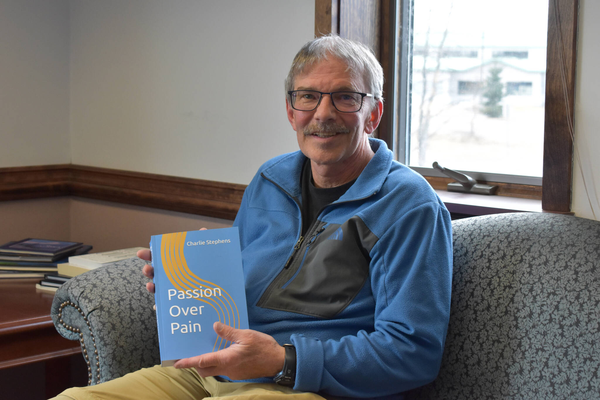 Charlie Stephens sits with a copy of his book, "Passion Over Pain" on Monday, May 1, 2023, in the Peninsula Clarion offices in Kenai, Alaska. (Jake Dye/Peninsula Clarion)