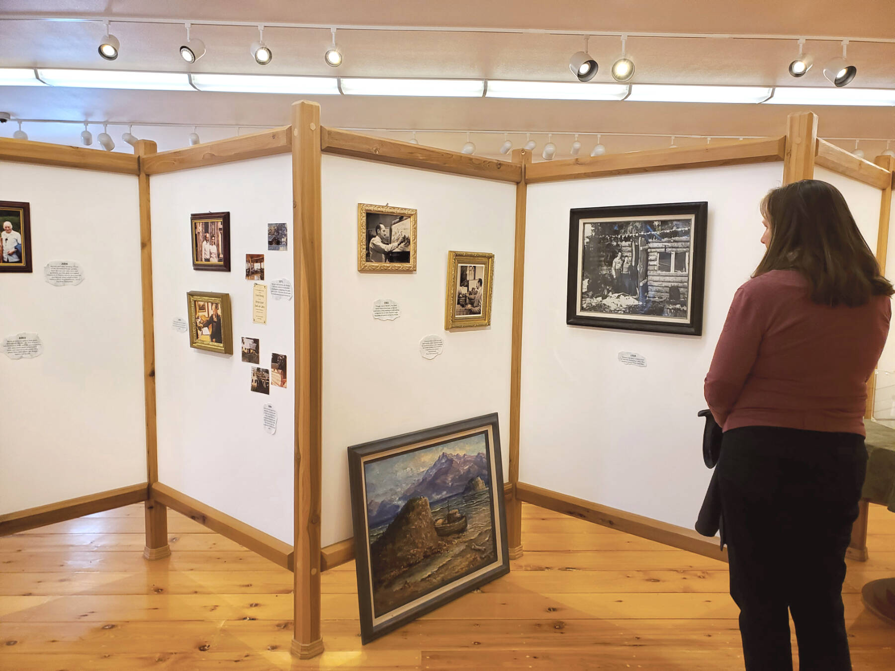 An attendee of the invitational gathering on Saturday, April 29, 2023 at the Norman Lowell Art Gallery in Anchor Point, Alaska views a display of photographs and information on Lowell’s life and career. Photo by Delcenia Cosman