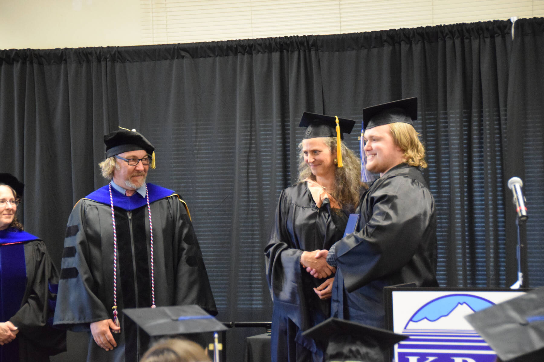 Tanner Saulls (right) is awarded his high school equivalency diploma by Kachemak Bay Campus Adult Education Coordinator Michelle Waclawski (center) during the 2023 KBC Commencement on Wednesday, May 10, 2023, in Homer, Alaska. (Photo by Delcenia Cosman/Homer News)