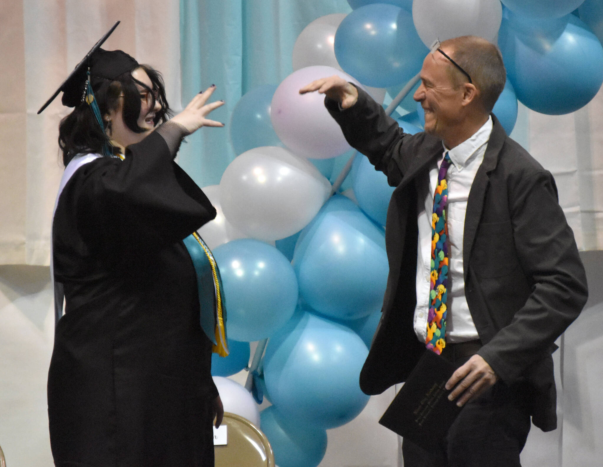 Fiona Wolfe-Jones and teacher Tad DeGray conduct a special handshake before Wolfe-Jones received her diploma at the River City Academy graduation Wednesday, May 17, 2023, at River City Academy inside Skyview Middle School just outside of Soldotna, Alaska. (Photo by Jeff Helminiak/Peninsula Clarion)