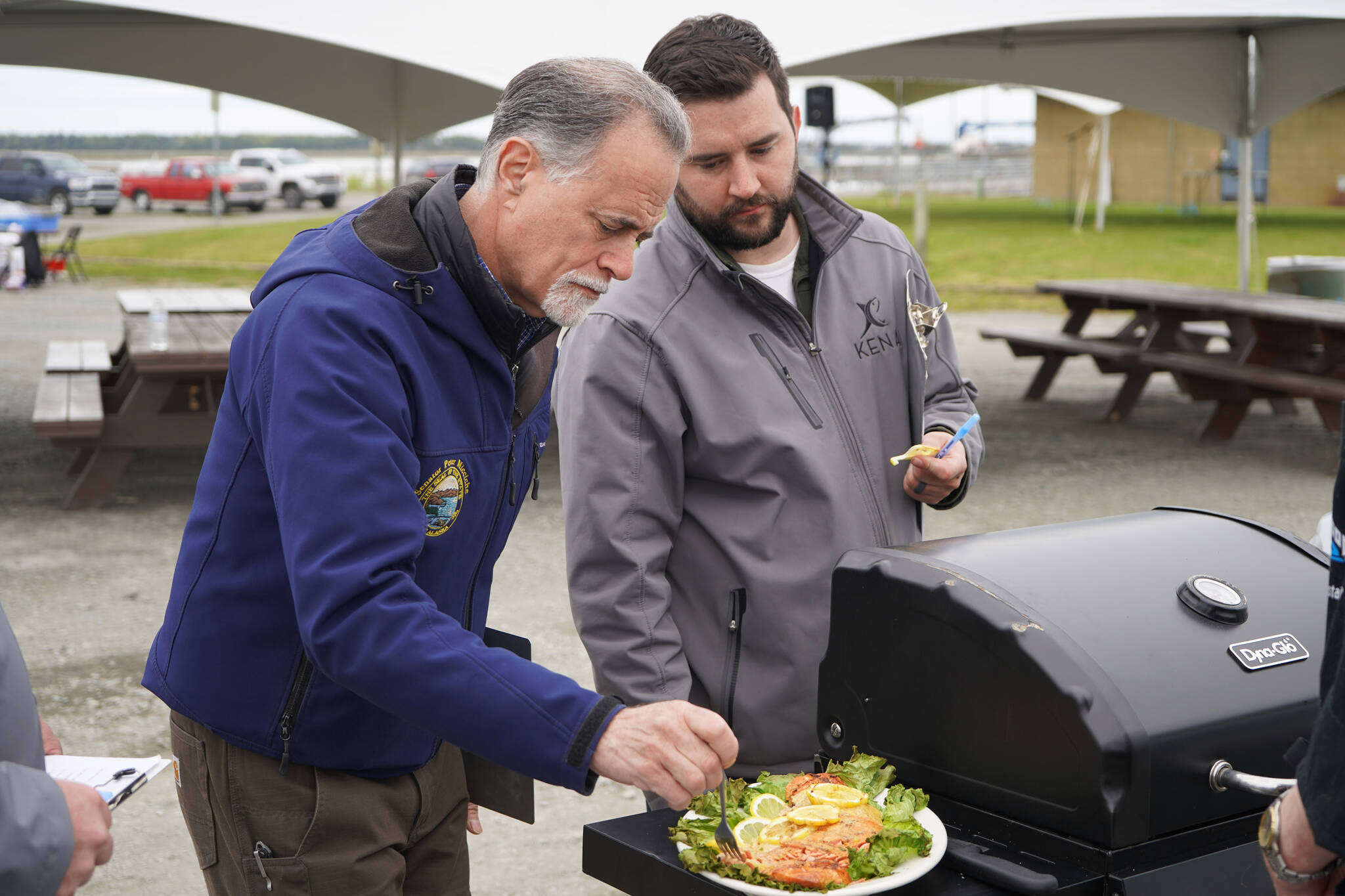 Judges Peter Micciche and Tyler Best sample a salmon dish prepared by chef Lastan Williams of The Catch at Return of the Reds on Saturday, June 3, 2023, at the Kenai City Dock in Kenai, Alaska. (Jake Dye/Peninsula Clarion)