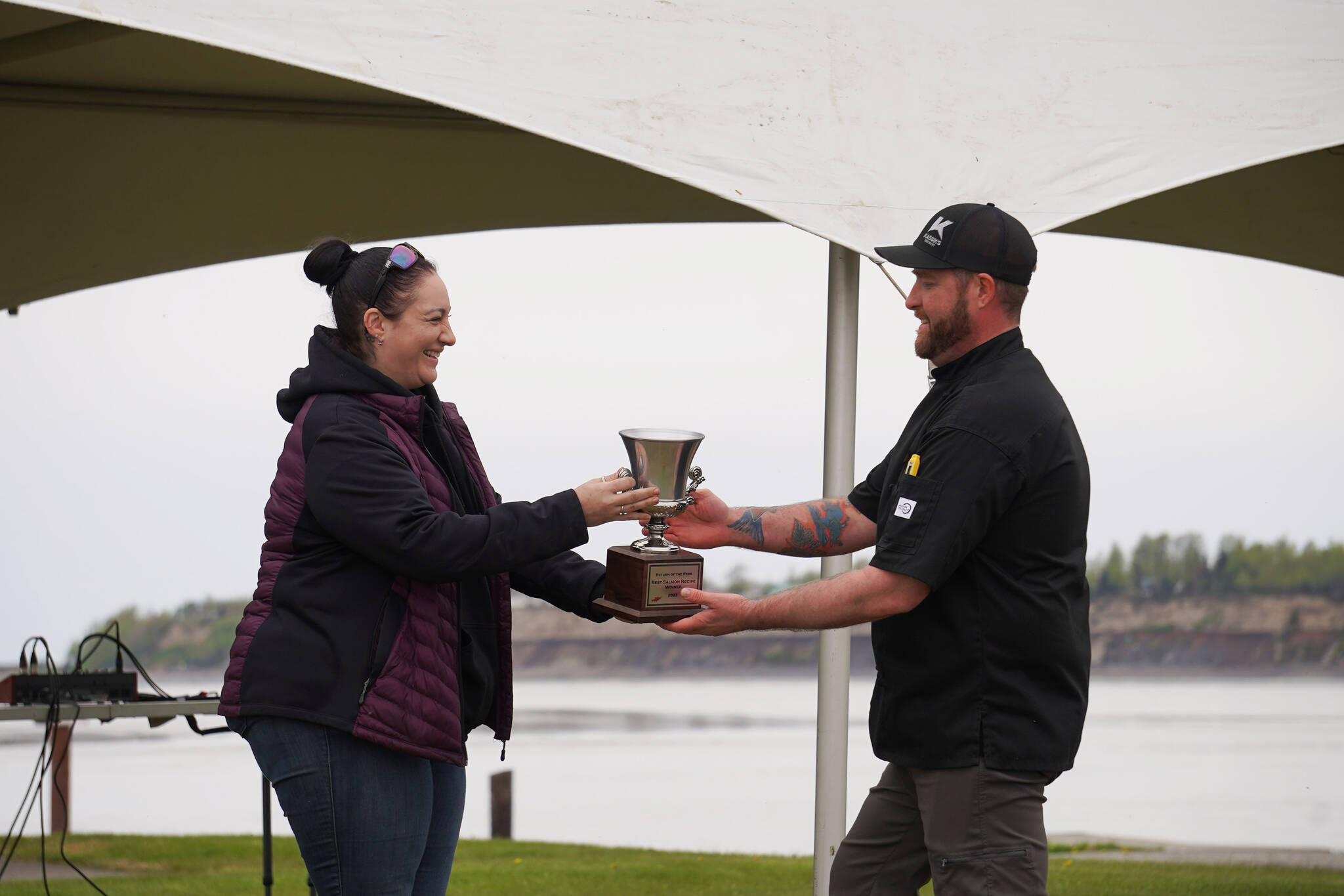 Kenai Chamber of Commerce Executive Director Samantha Springer hands a trophy to Kenai Peninsula Food Bank head chef Stephen Lamm for winning the Return of the Reds Best Salmon Recipe competition on June 3, 2023, at the Kenai City Docks in Kenai, Alaska. (Jake Dye/Peninsula Clarion)