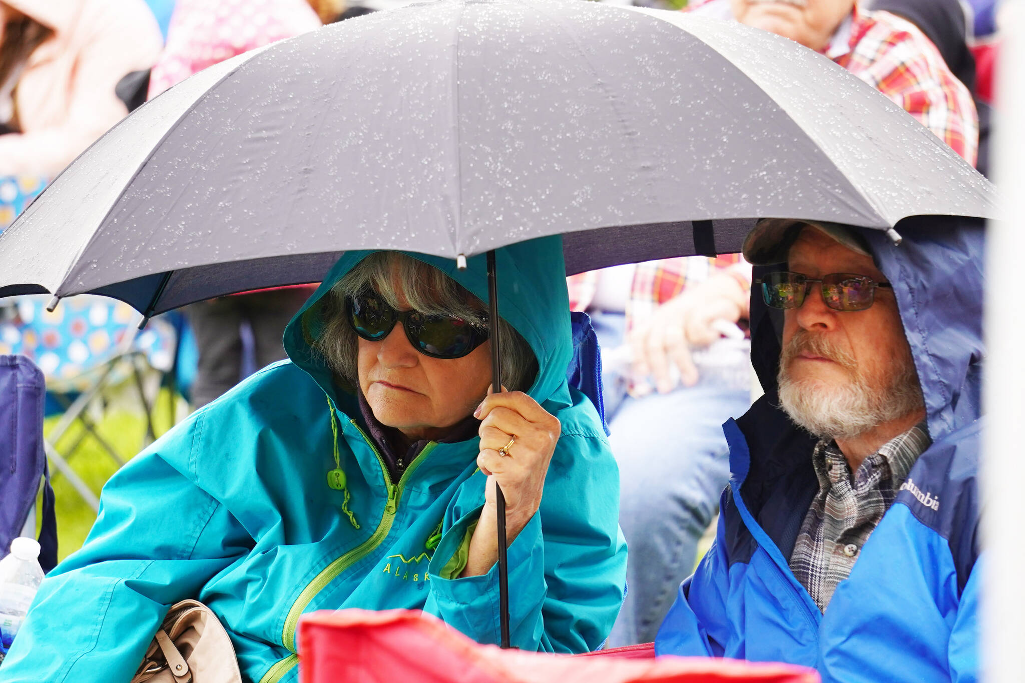 Attendees huddle under umbrellas and in raincoats during the Levitt AMP Soldotna Music Series on Wednesday, June 7, 2023, at Soldotna Creek Park in Soldotna, Alaska. (Jake Dye/Peninsula Clarion)