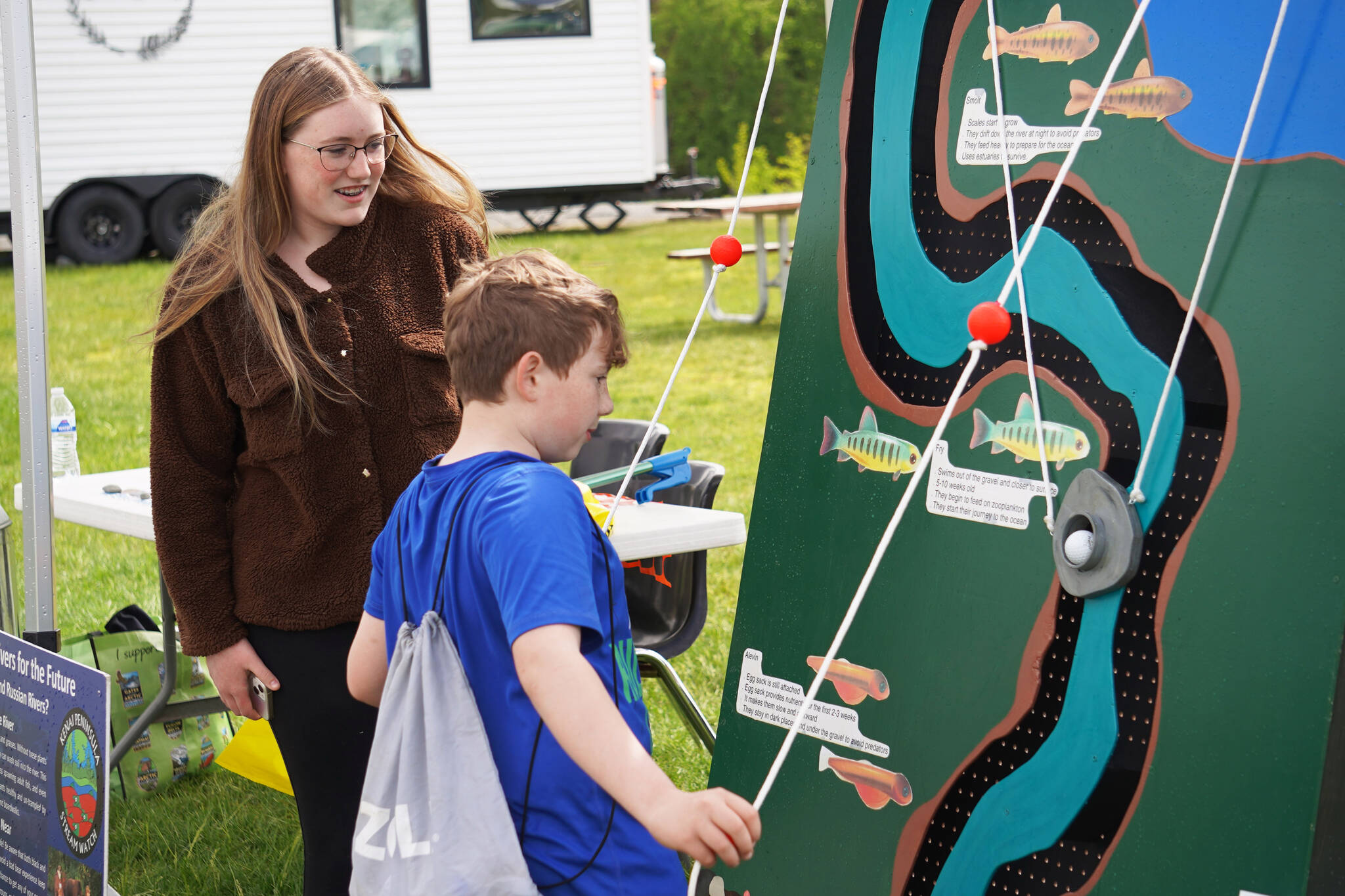 Emerson Kapp, second-place winner of the 2023 Caring for the Kenai competition, directs participants in the use of her project, the Kenai Peninsula Maze Board during the Kenai River Festival on Friday, June 9, 2023, at Soldotna Creek Park in Soldotna, Alaska. (Jake Dye/Peninsula Clarion)