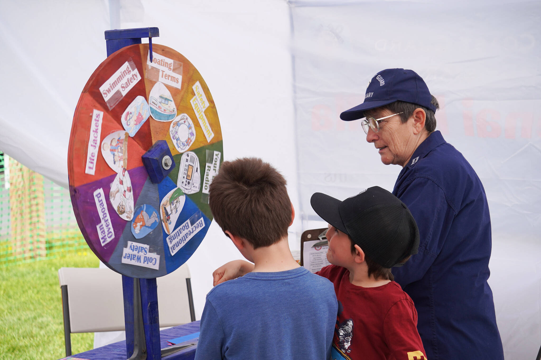Kids spin a wheel and answer boating questions at a booth run by the U.S. Coast Guard Auxiliary during the Kenai River Festival on Friday, June 9, 2023, at Soldotna Creek Park in Soldotna, Alaska. (Jake Dye/Peninsula Clarion)