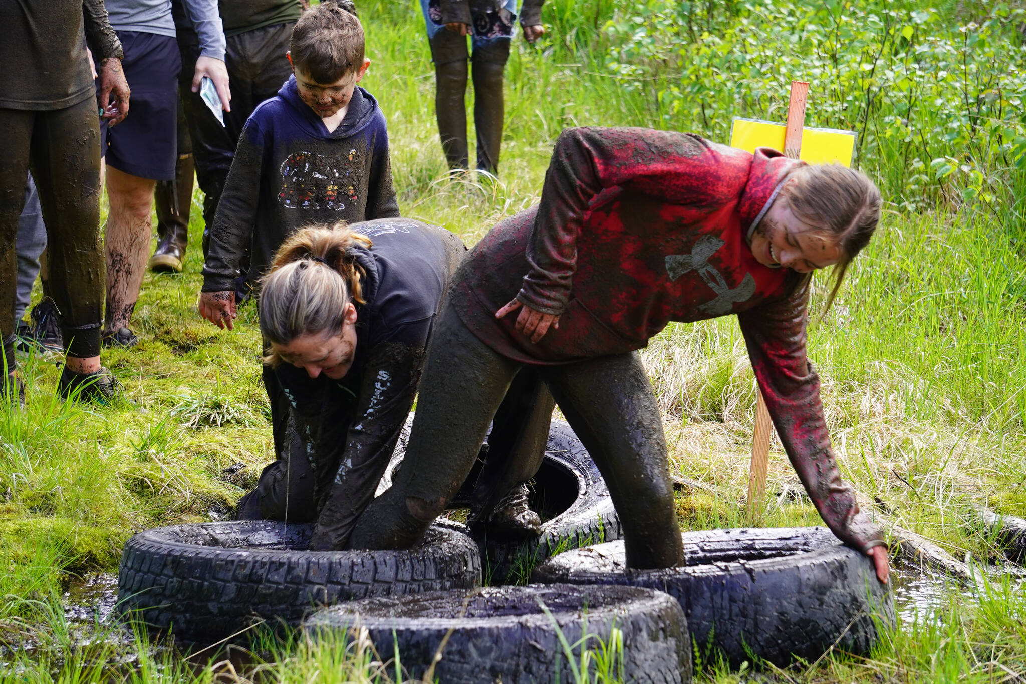 It takes more than one to free a trapped foot during the KDLL Mud Run at Tsalteshi Trails in Soldotna, Alaska, on Friday, June 16, 2023. (Jake Dye/Peninsula Clarion)