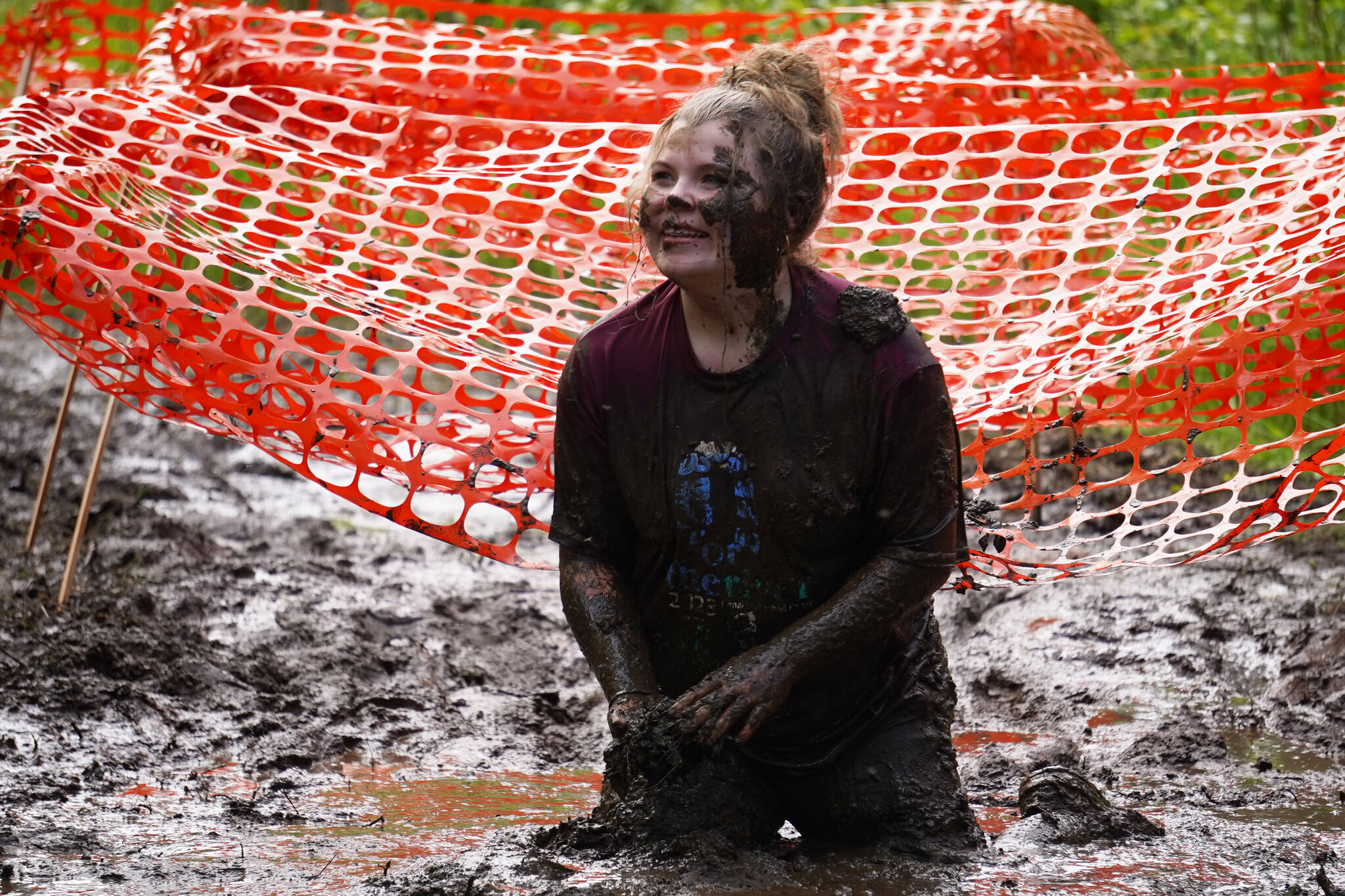 A contestant sits in the mud with a smile during the KDLL Mud Run at Tsalteshi Trails in Soldotna, Alaska, on Friday, June 16, 2023. (Jake Dye/Peninsula Clarion)