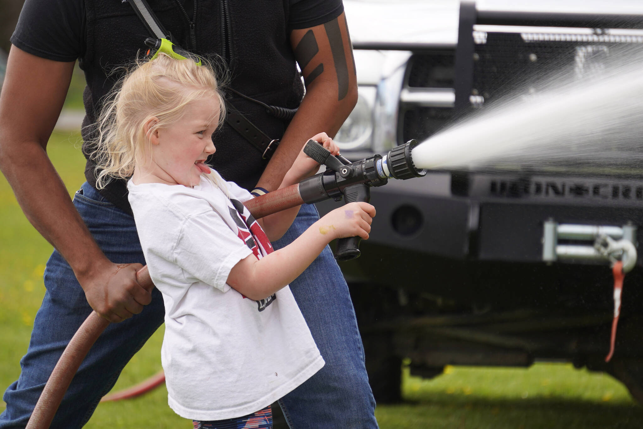 Sarah Chesser works a Nikiski Fire Department hose during Family Fun in the Midnight Sun on Saturday, June 17, 2023, at the Nikiski Community Recreation Center in Nikiski, Alaska. (Jake Dye/Peninsula Clarion)