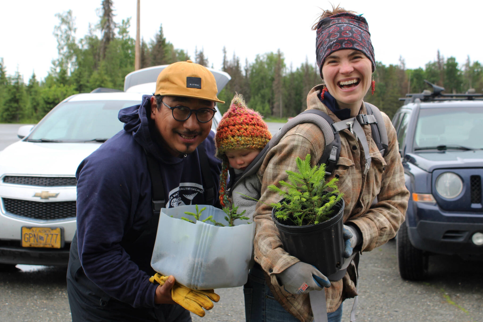 From left, David Knight, Skadi Vadla and Kaitlin Vadla hold repotted white spruce trees near the Soldotna Regional Sports Complex on Tuesday, June 27, 2023 in Soldotna, Alaska. (Ashlyn O’Hara/Peninsula Clarion)