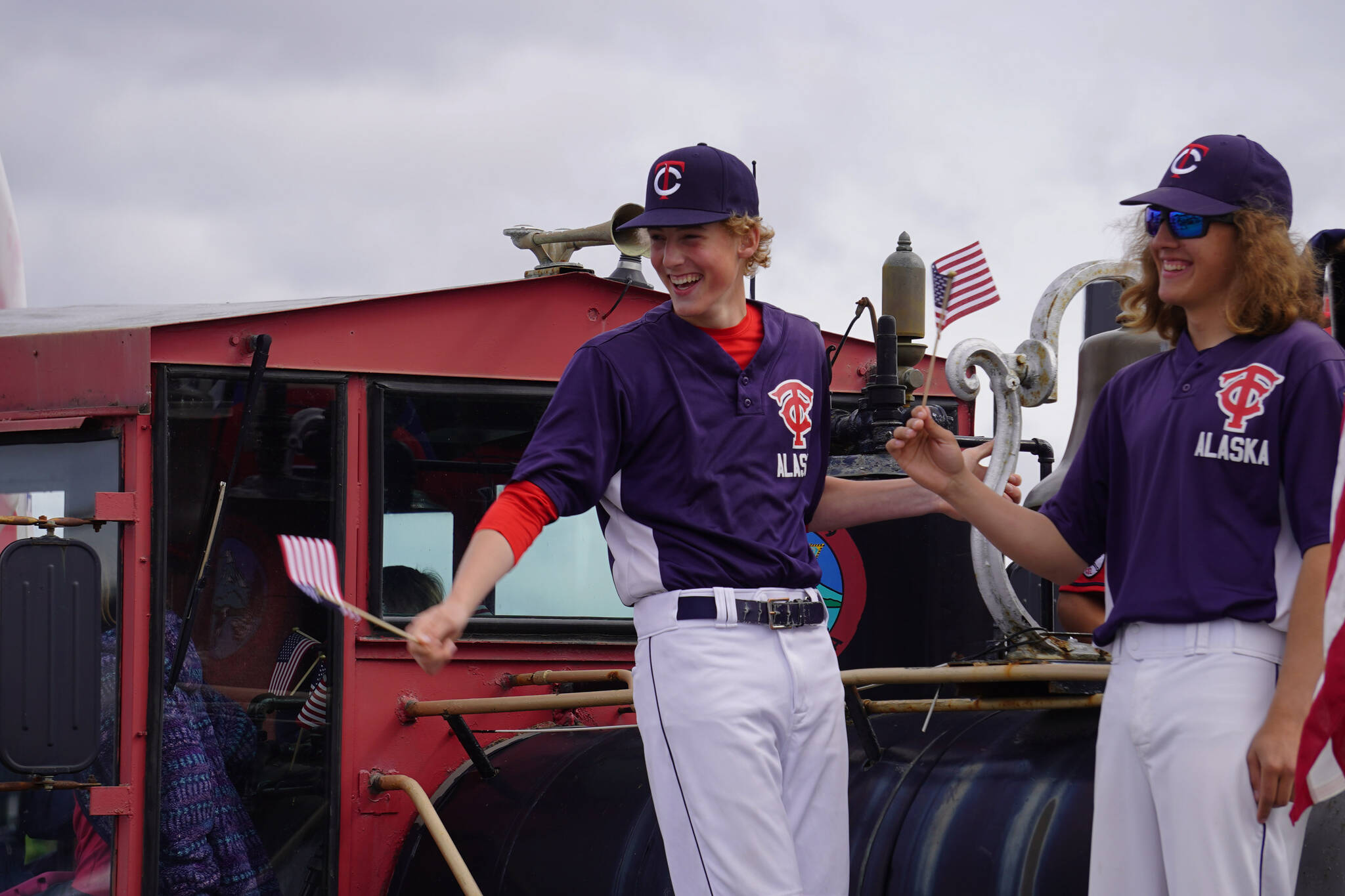 Players for the American Legion Twins smile and wave as the Fourth of July Parade moves down South Willow Street in Kenai, Alaska on Tuesday, July 4, 2023. (Jake Dye/Peninsula Clarion)