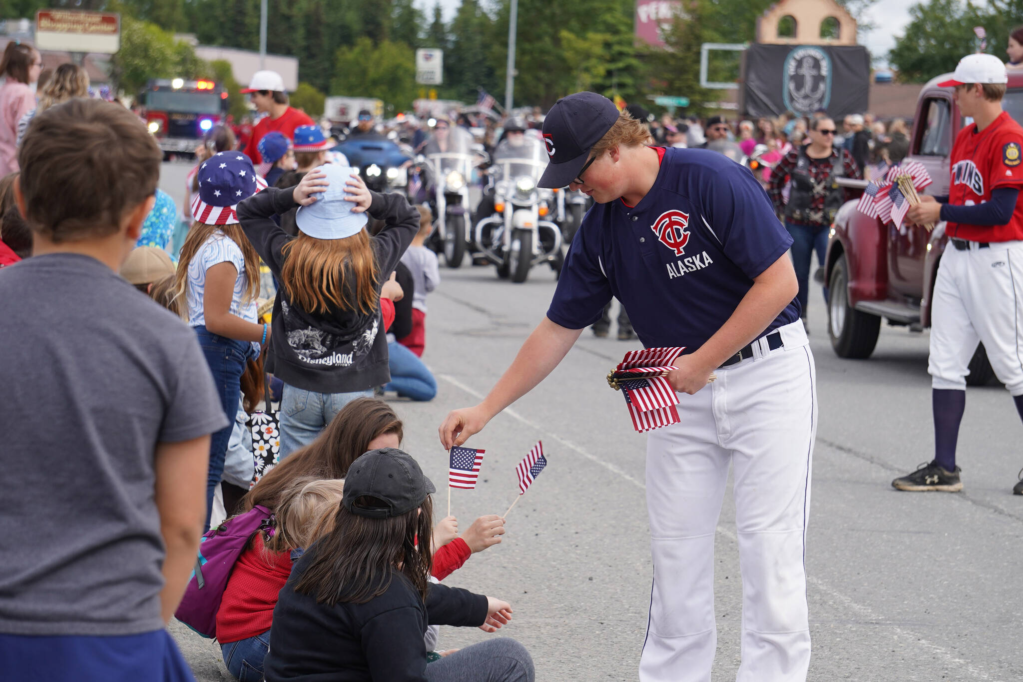 A player for the American Legion Twins hands out flags as the Fourth of July Parade moves down South Willow Street in Kenai, Alaska on Tuesday, July 4, 2023. (Jake Dye/Peninsula Clarion)