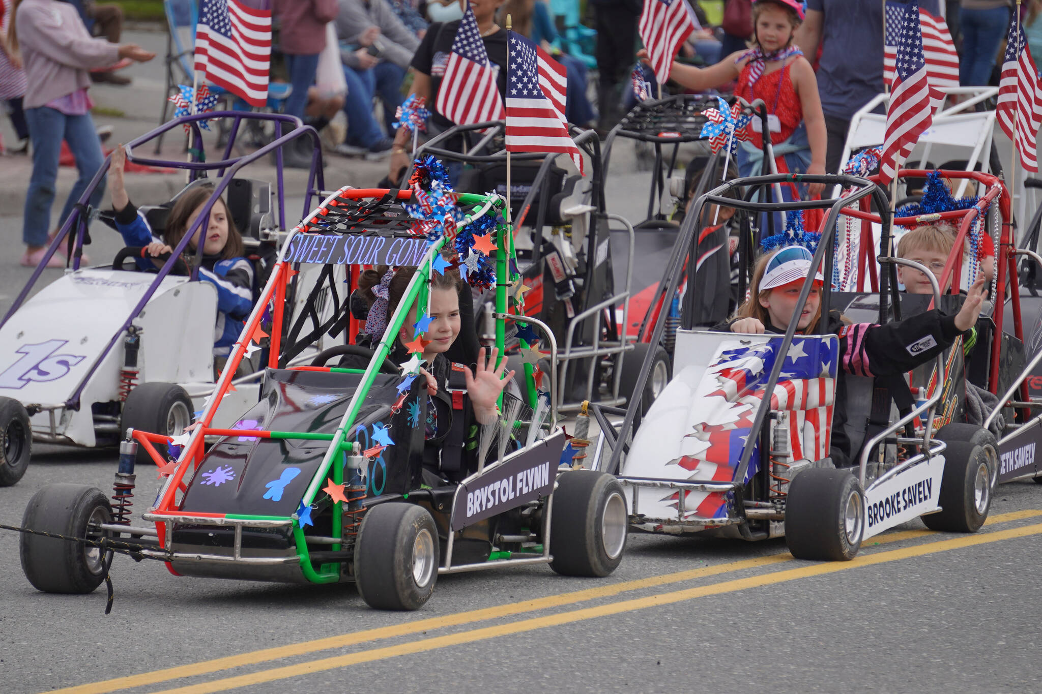 Kids ride carts and wave as the Fourth of July Parade moves down the Kenai Spur Highway in Kenai, Alaska on Tuesday, July 4, 2023. (Jake Dye/Peninsula Clarion)
