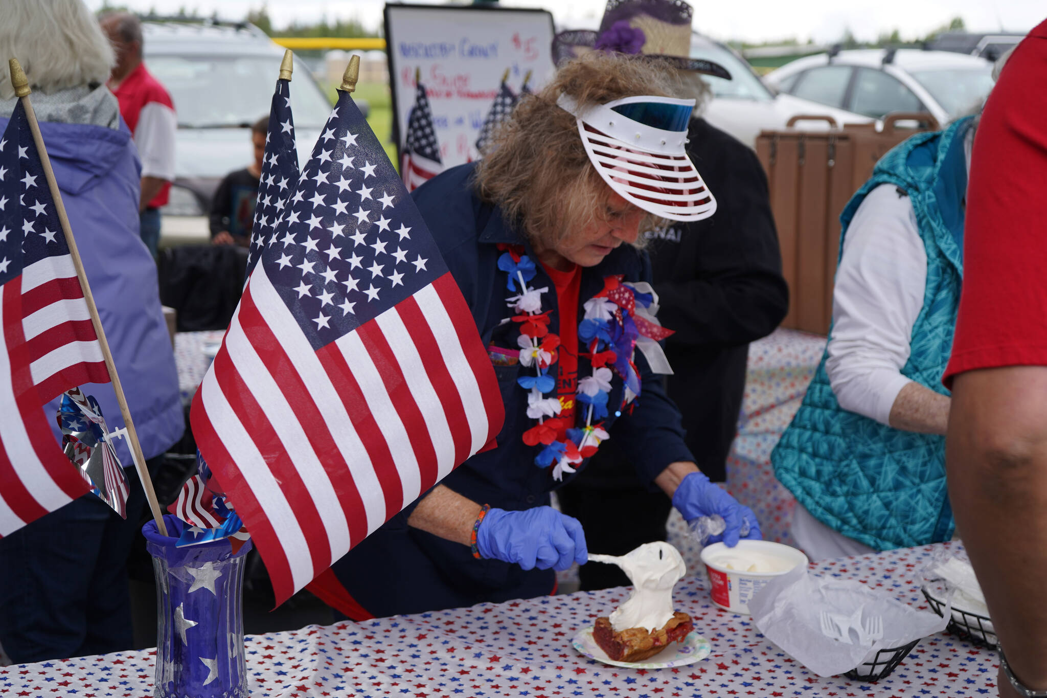 A member of the Kenai Senior Center administers a healthy dollop of cool whip onto a slice of strawberry rhubarb pie during Fourth of July festivities at the softball greenstrip in Kenai, Alaska on Tuesday, July 4, 2023. (Jake Dye/Peninsula Clarion)