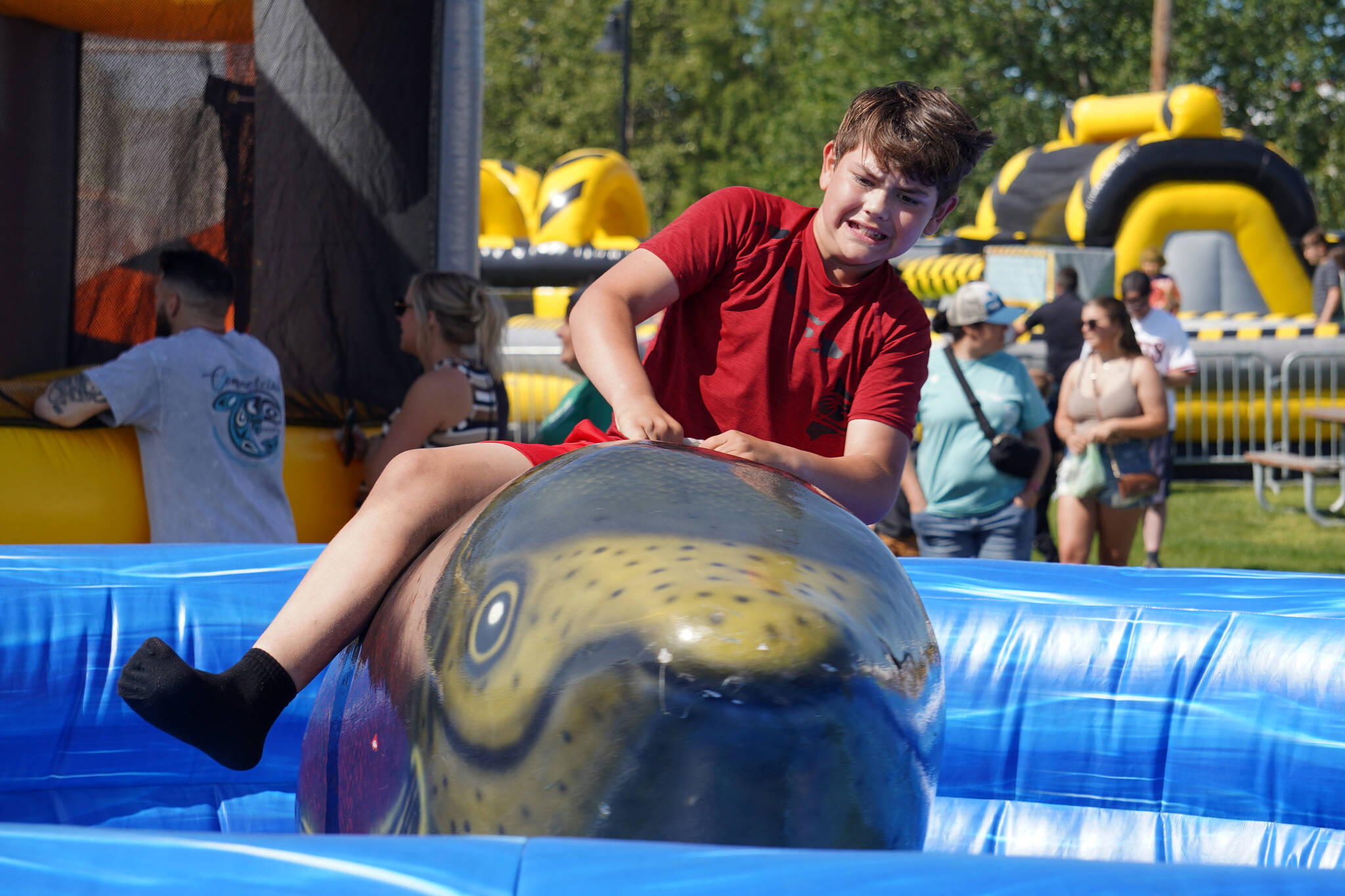 Owen McWilliams hangs tightly onto a mechanical salmon at the Progress Days Fair at Soldotna Creek Park in Soldotna, Alaska on Saturday, July 22, 2023. (Jake Dye/Peninsula Clarion)