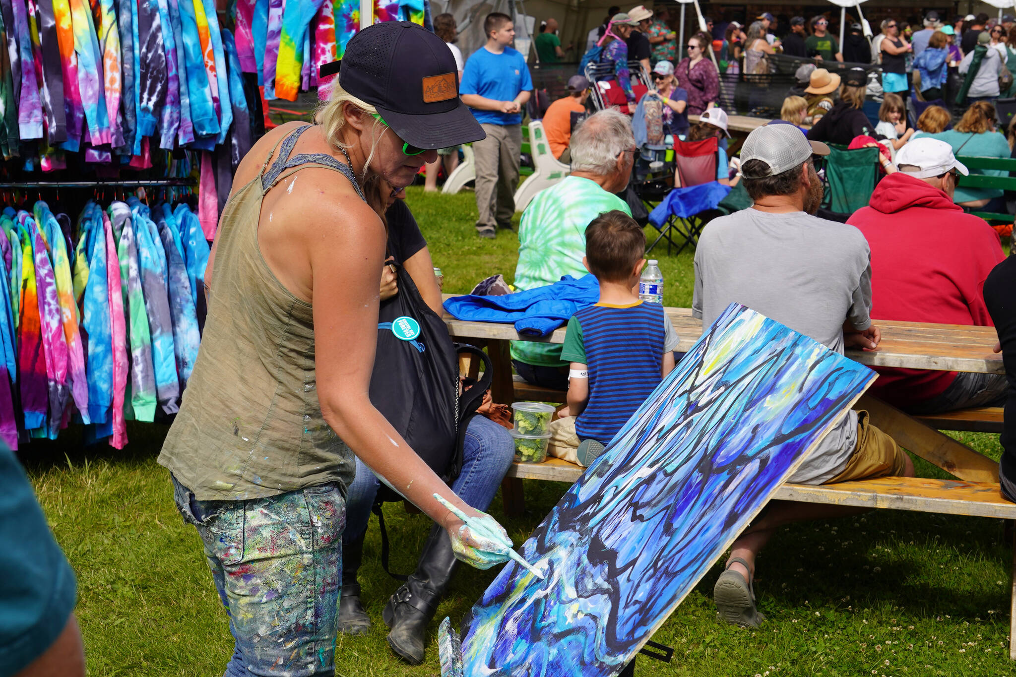 Chelsea Jones applies paint to canvas within eyesight of the Ocean Stage at Salmonfest in Ninilchik, Alaska, on Friday, Aug. 4, 2023. (Jake Dye/Peninsula Clarion)