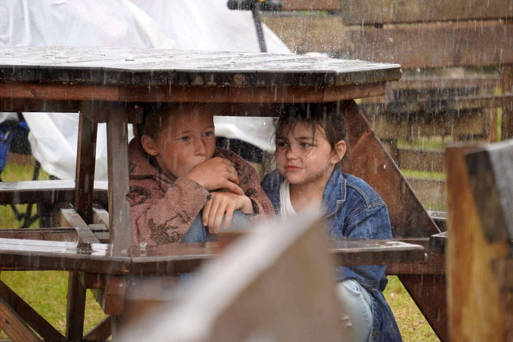 Children shelter from the rain under a picnic bench at the Kenai Peninsula Fair in Ninilchik, Alaska, on Friday, Aug. 11, 2023. (Jake Dye/Peninsula Clarion)