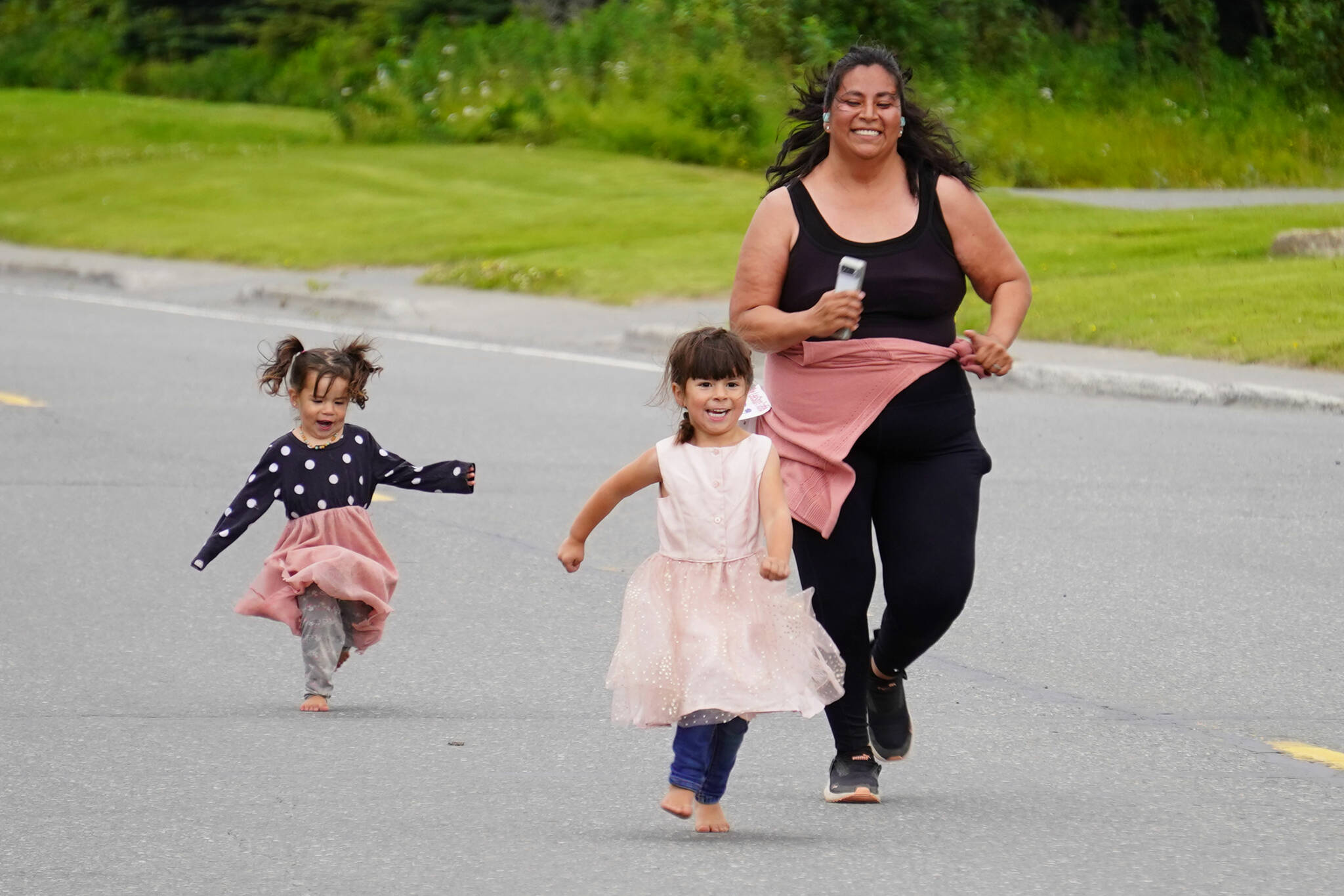 A participant, joined by children, races to the finish chute of the 34th Annual Kenai Peninsula Violence Free Community Run in Kenai, Alaska, on Saturday, Aug. 12, 2023. (Jake Dye/Peninsula Clarion)