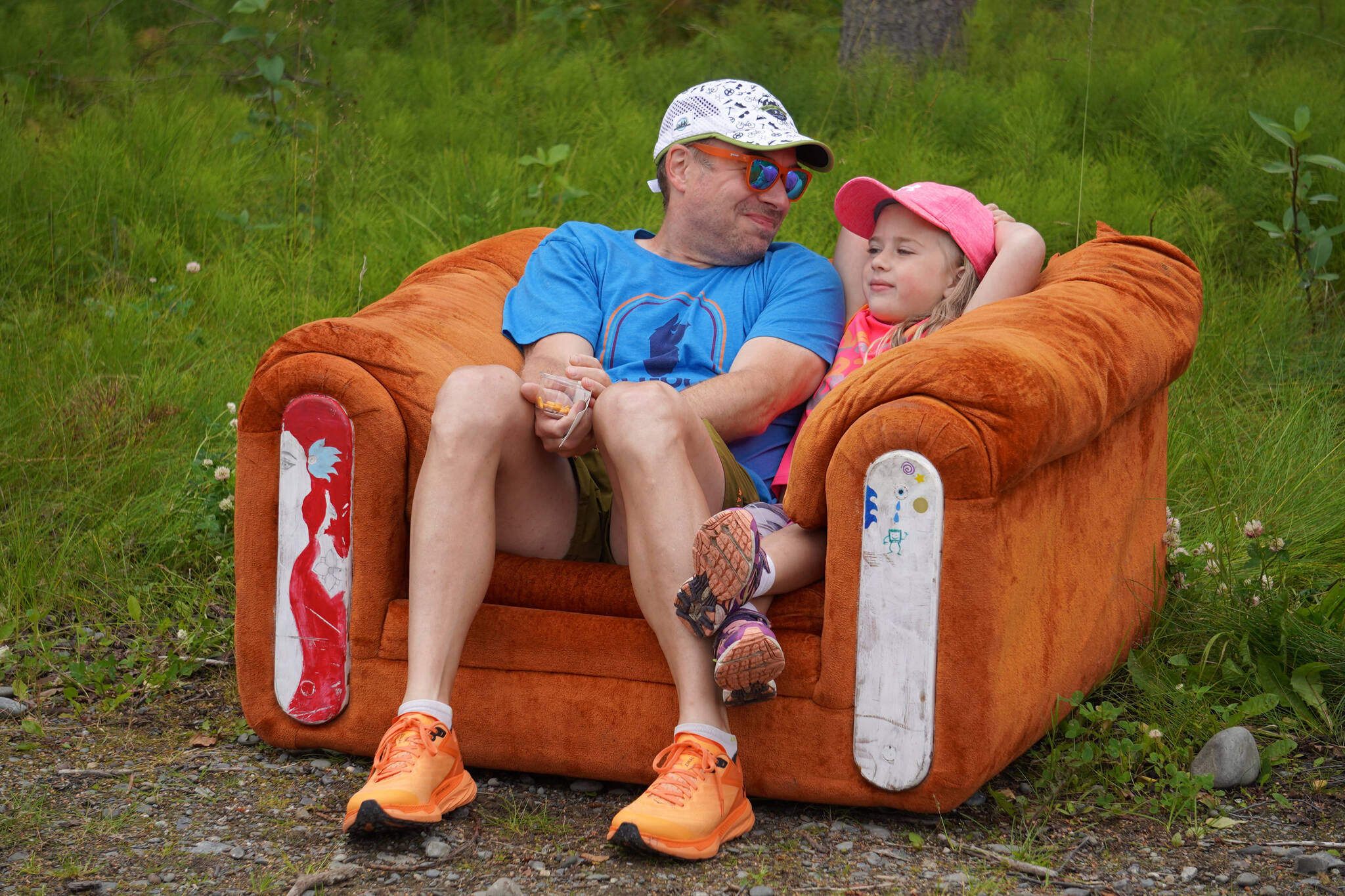 Jamie and Clara Nelson take a well-deserved rest on a couch during the Brewery to Bathroom .5K at Kenai River Brewing in Soldotna, Alaska, on Sunday, Aug. 13, 2023. (Jake Dye/Peninsula Clarion)