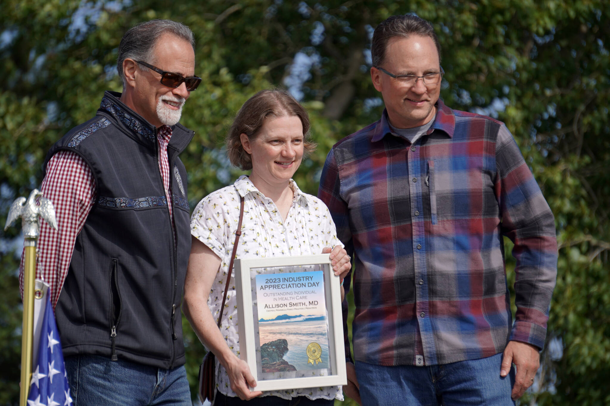 Dr. Allison Smith, center, receives the Outstanding Individual in Health Care Award from Kenai Peninsula Borough Mayor Peter Micciche and Rep. Ben Carptenter, R-Nikiski, during Industry Appreciation Day festivities at the Kenai softball greenstrip on Saturday, Aug. 19, 2023. (Jake Dye/Peninsula Clarion)